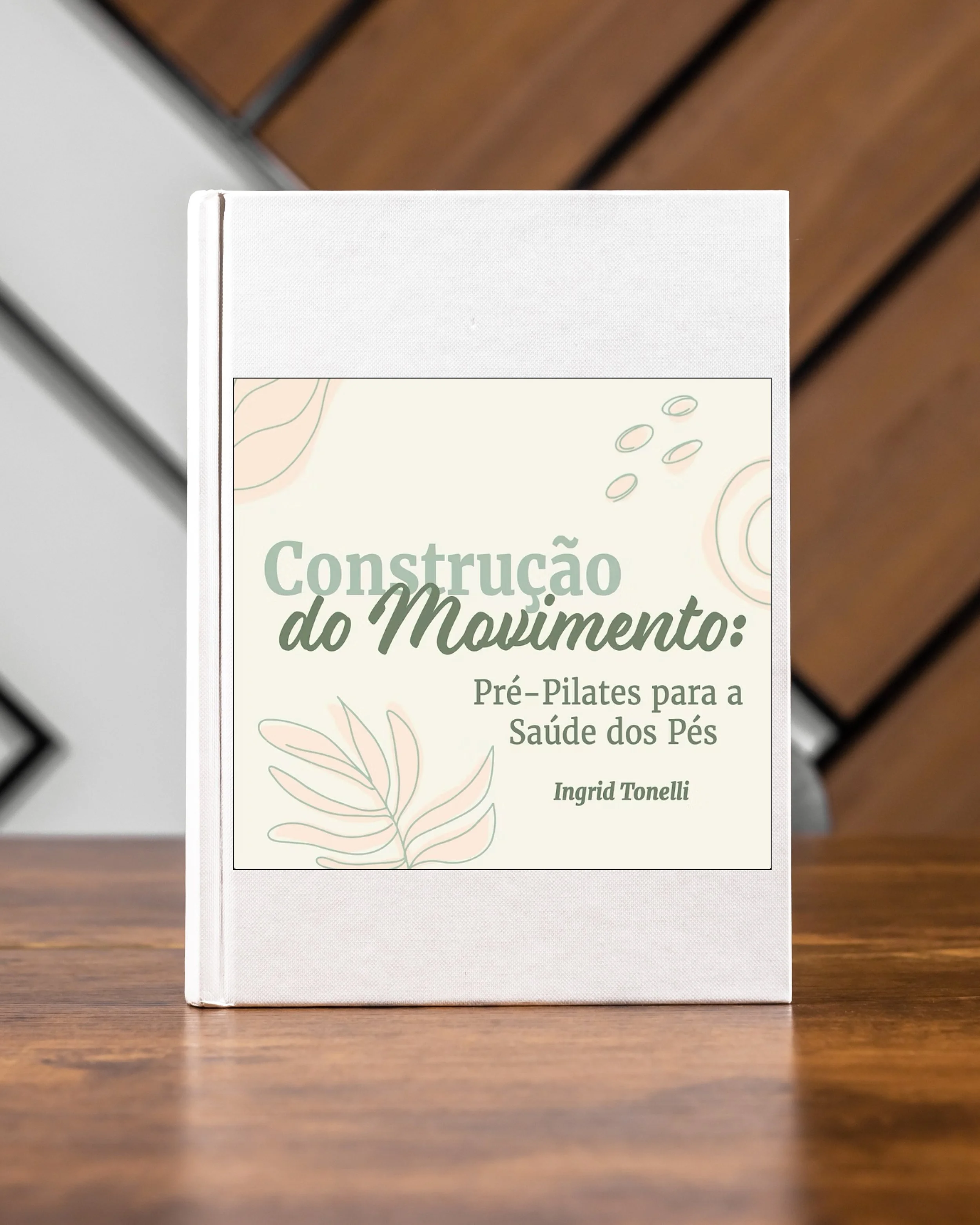 Book titled 'Construção do Movimento: Pré-Pilates para a Saúde dos Pés' by Ingrid Tonelli on a wooden table.