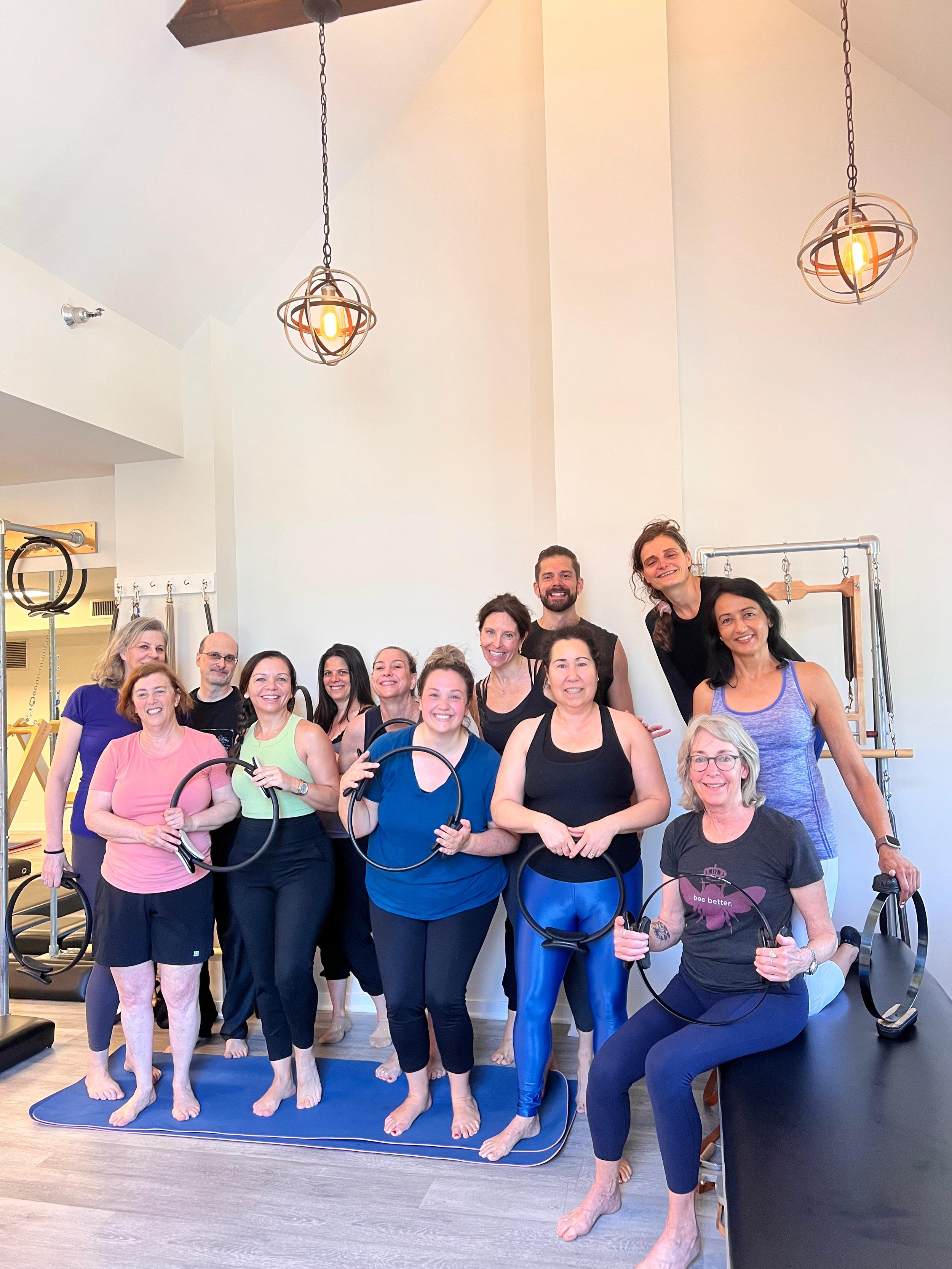 group of women and men participating in a fitness class in a gym, holding fitness rings, some standing on a yoga mat, smiling.