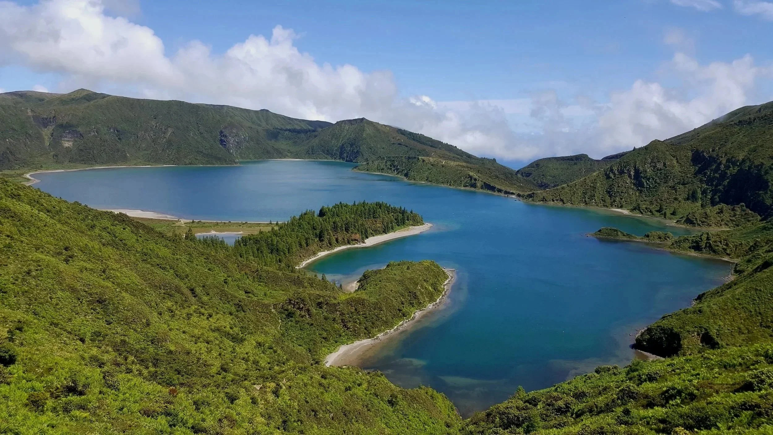 A scenic lake surrounded by lush green hills under a partly cloudy sky.