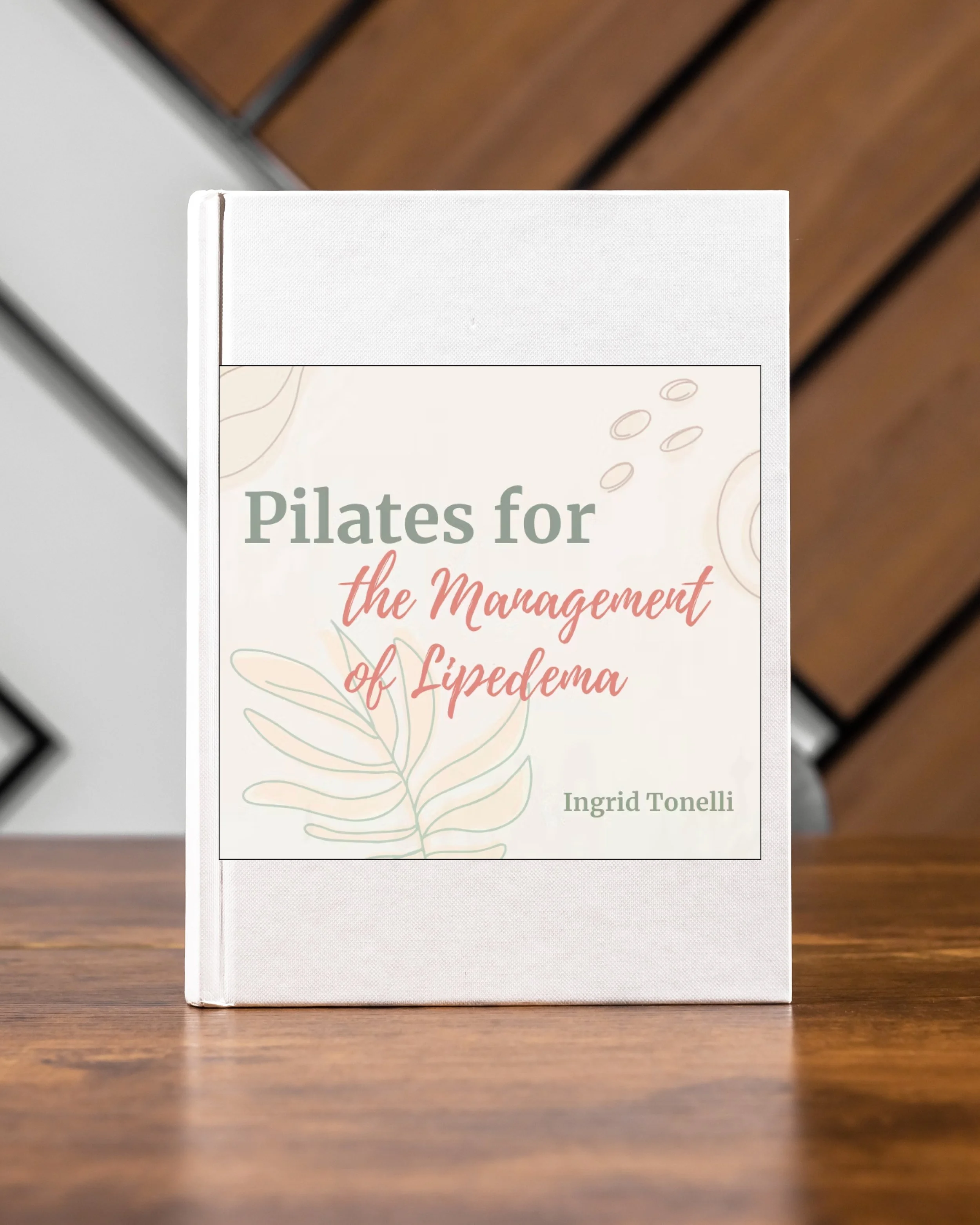Book titled 'Pilates for the Management of Lipedema' by Ingrid Tonelli sitting on a wooden surface.
