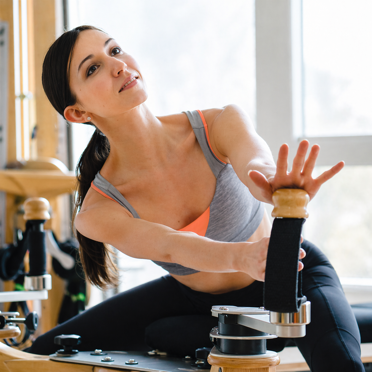 A woman exercising on specialized fitness equipment in a bright room with large windows.