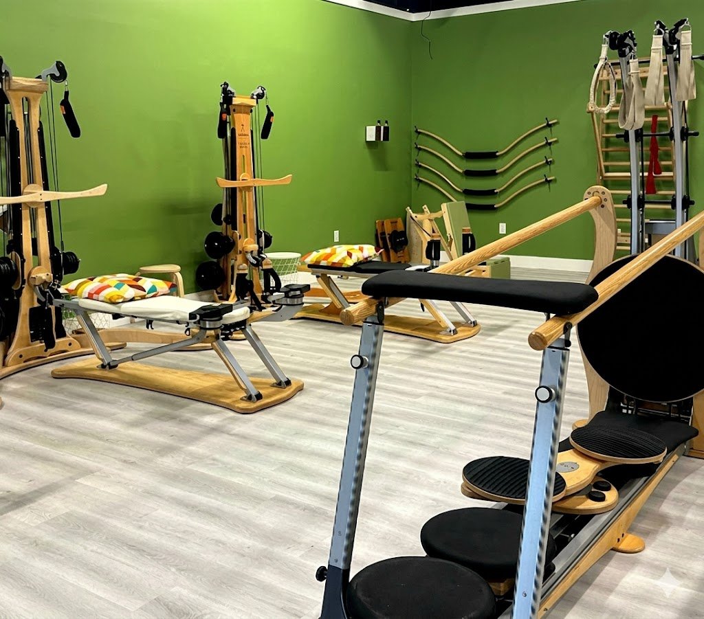 Pilates studio with wooden exercise equipment, mats, and resistance bands on a green wall.