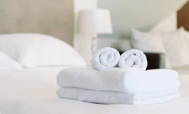 Set of neatly folded white towels on a bed in a hotel room.