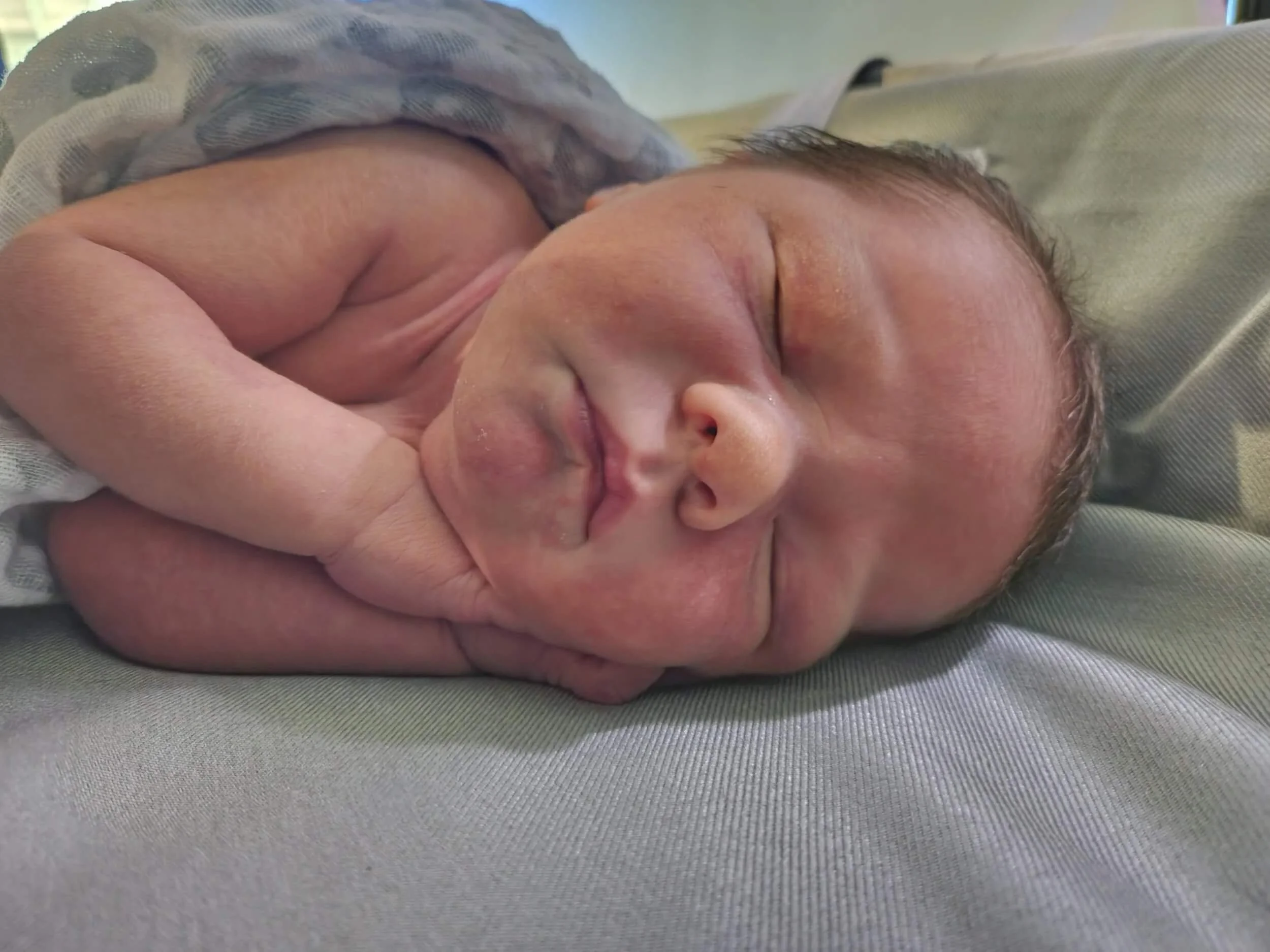 Close-up of a newborn baby sleeping peacefully on a soft surface, with eyes gently closed and a hand resting near the face.