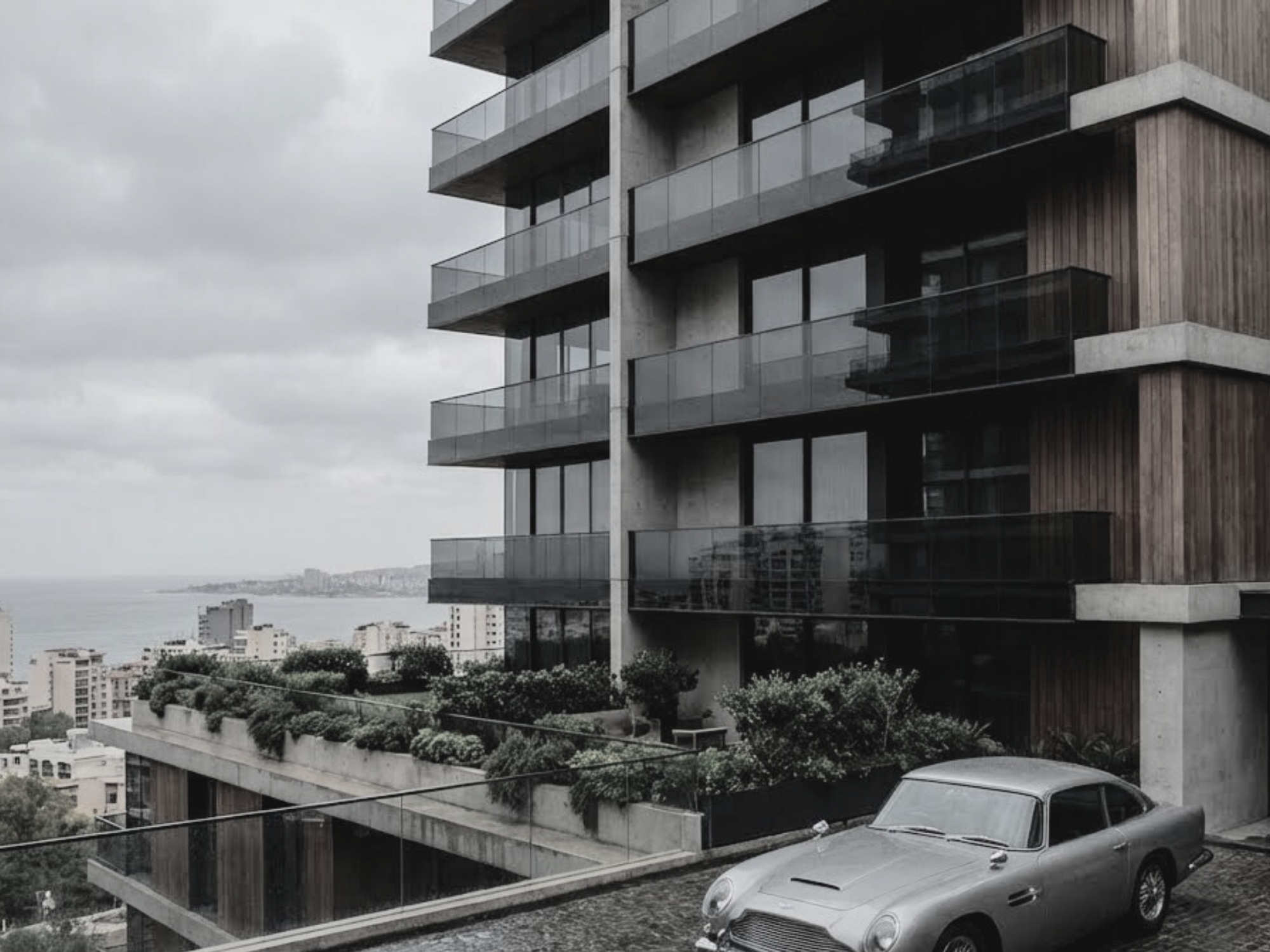 Modern apartment building with glass balconies and a driveway with a vintage silver car parked in front.
