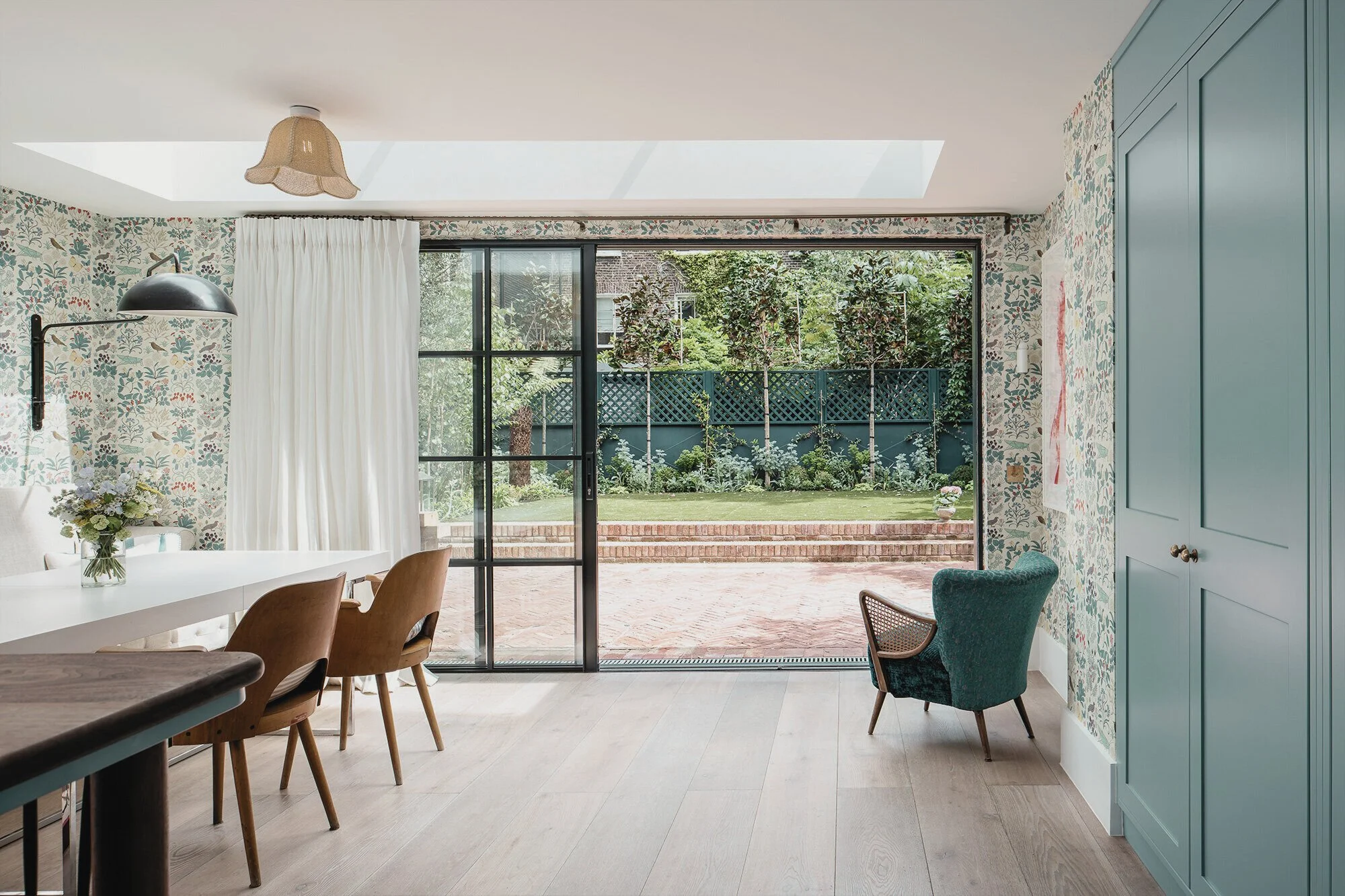 Bright outdoor backyard seen through sliding glass doors, with brick patio, green grass, and landscaped garden.