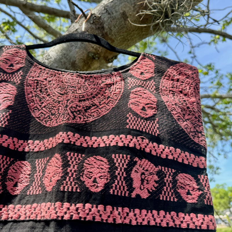 Close-up of pink and black patterned fabric hanging from a tree branch, with blue sky and green leaves in the background.