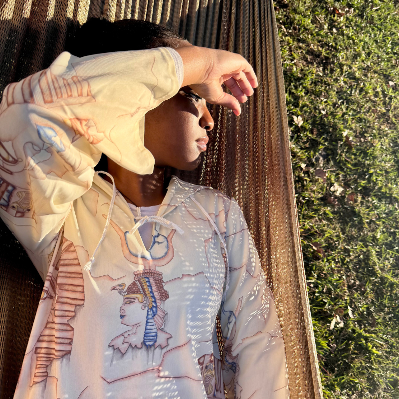 A young woman lying on a wooden lounge chair on grass, shielding her eyes from the sun with her hand.