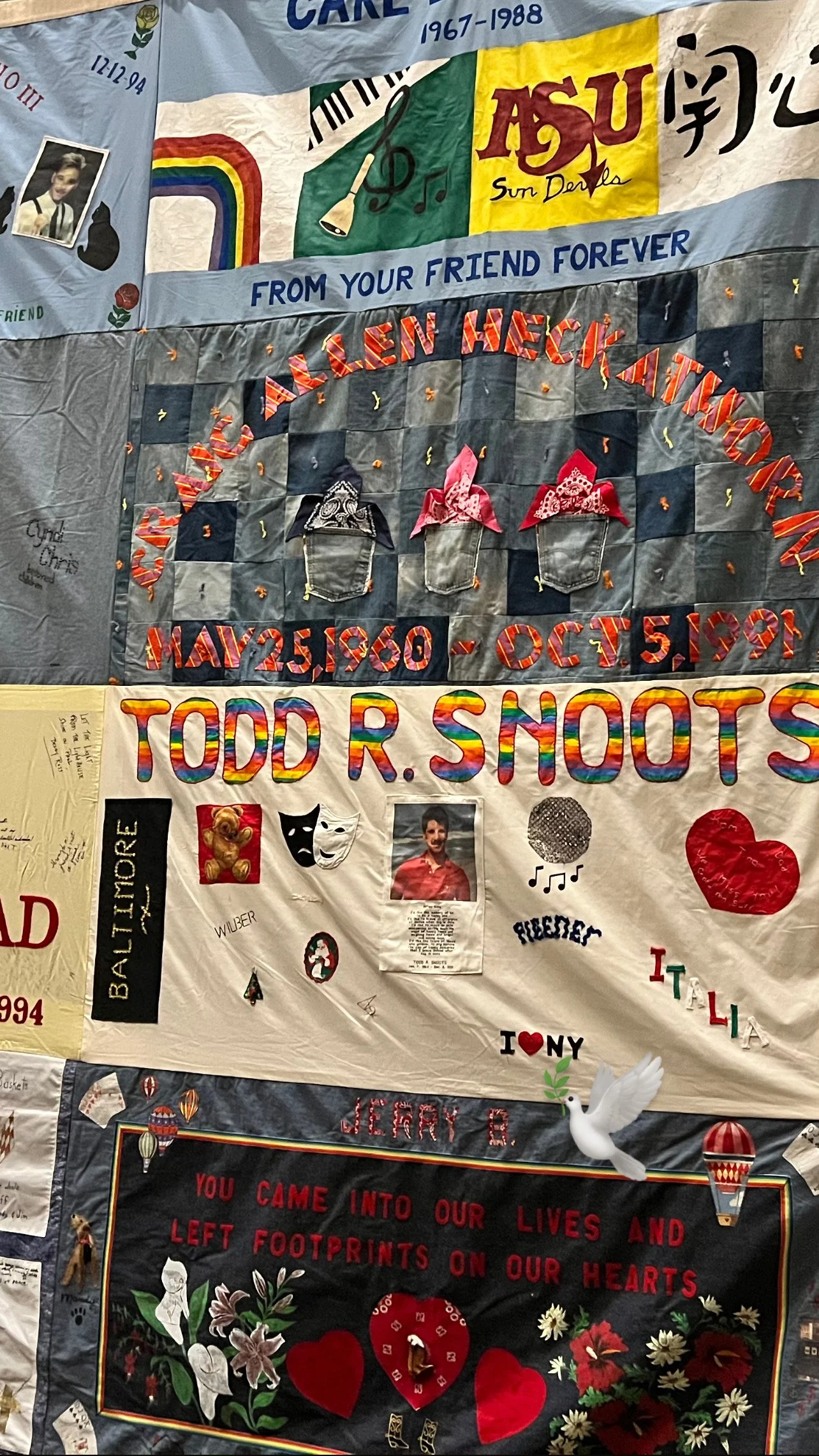 A collage of colorful fabric banners and posters celebrating the life and memory of loved ones. The banners feature names, dates, photos, and decorative elements such as flowers, hearts, and symbols, with messages of remembrance and tribute.