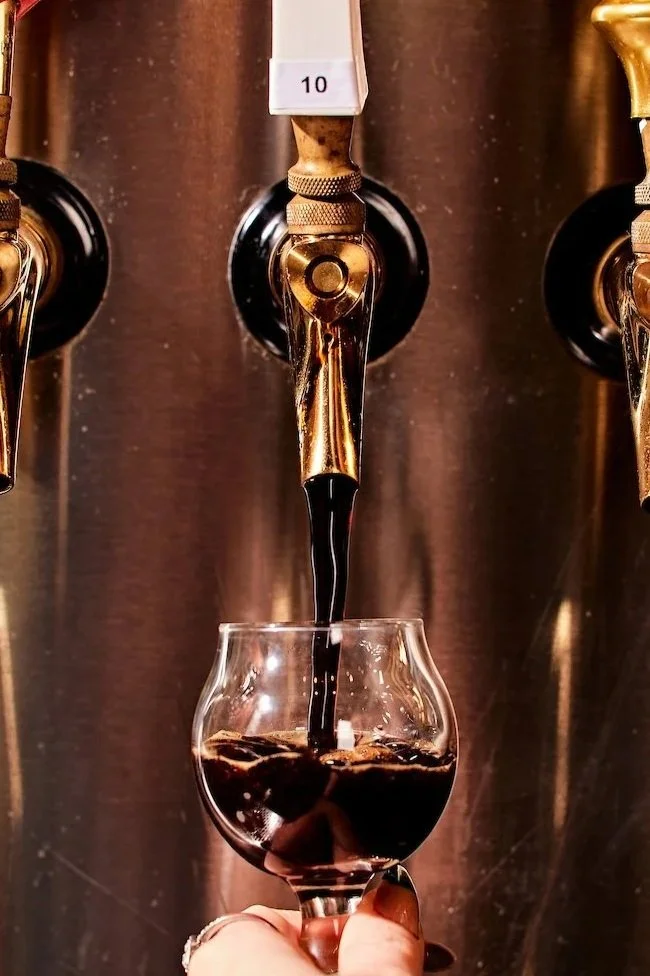A hand holding a glass under a tap pouring dark soda from a soda fountain machine.