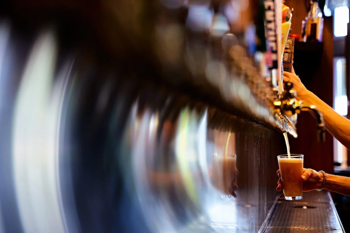 A person pouring beer from a tap into a glass at a bar.