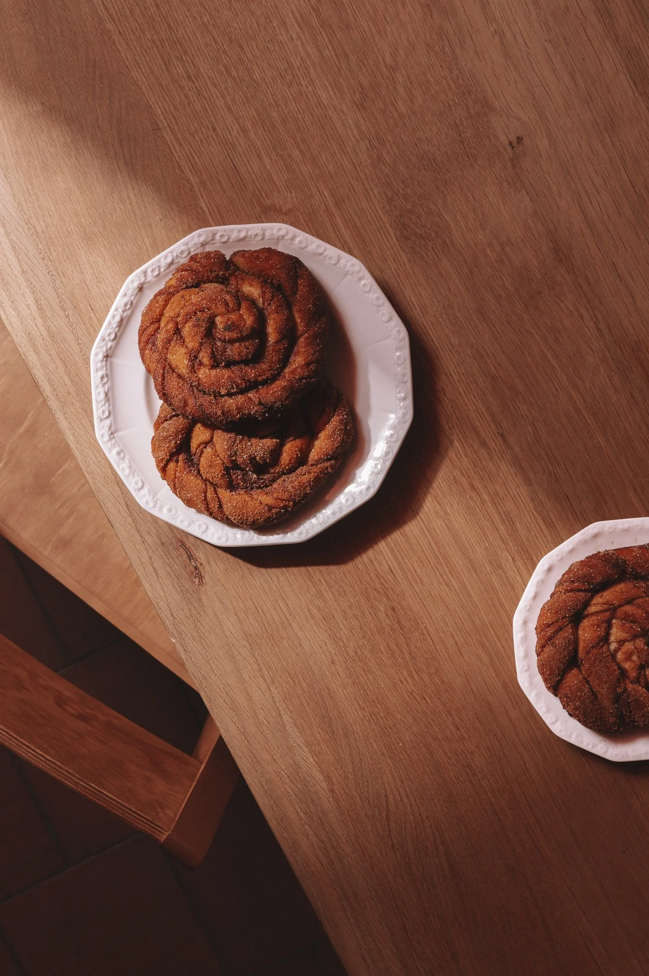 Two cinnamon rolls on a white decorative plate on a wooden table.
