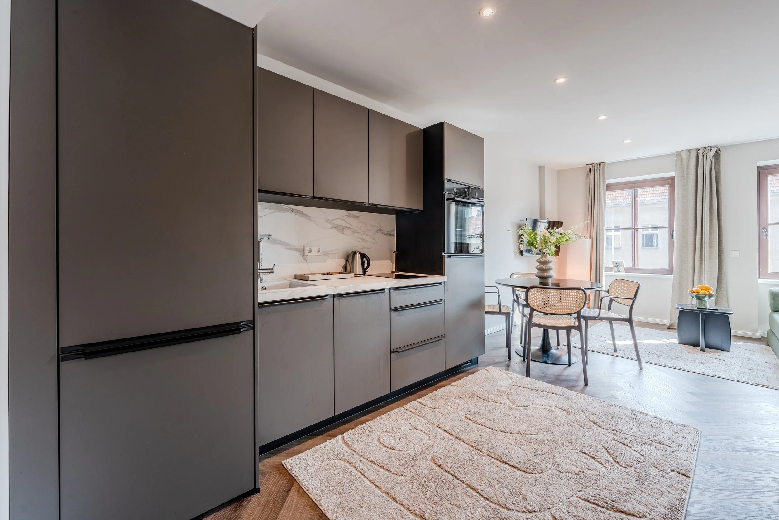 Modern kitchen and dining area with gray cabinets, marble backsplash, round table with four chairs, large window, and beige rug.