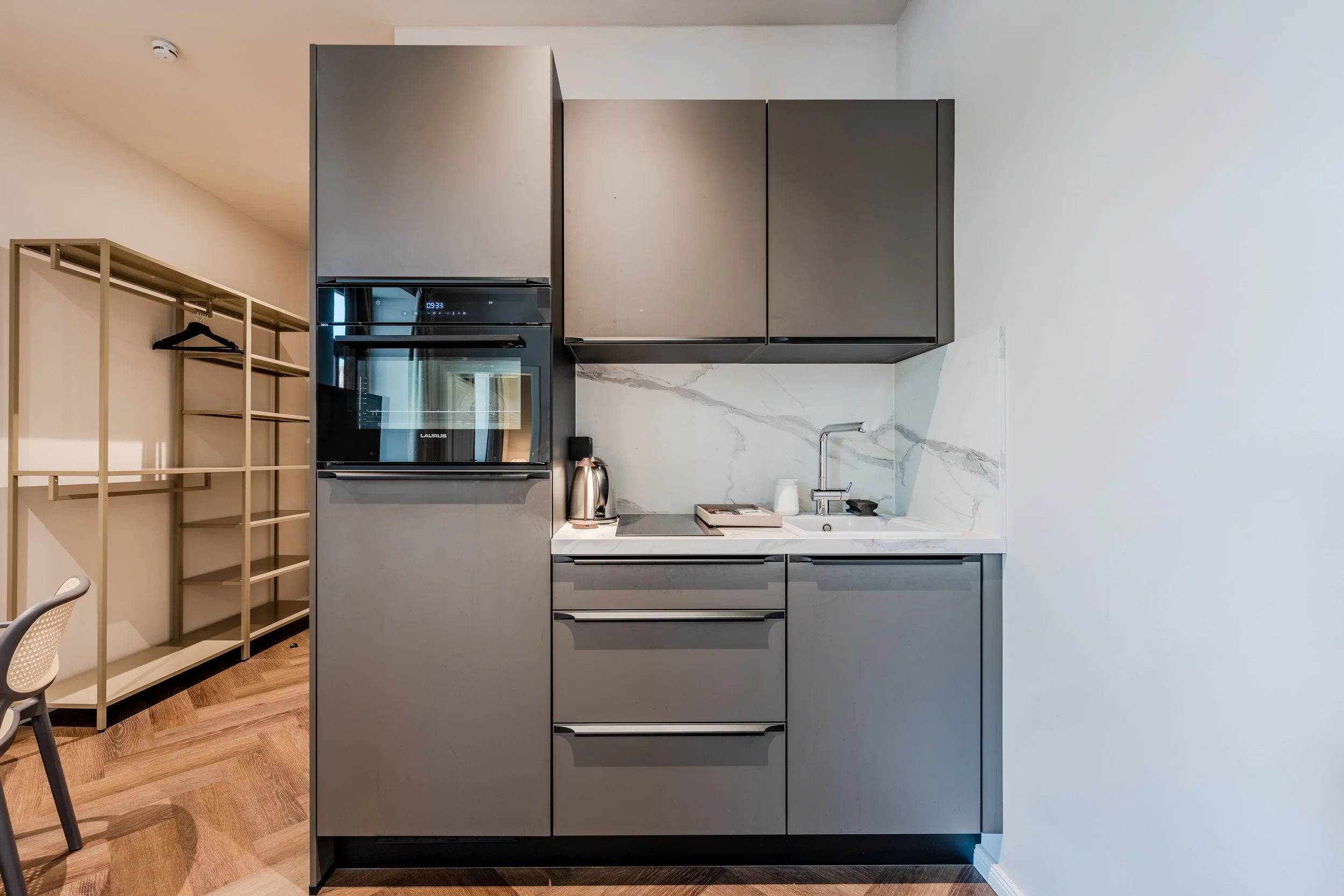 Modern kitchen with gray cabinetry, a built-in oven, marble backsplash, a small sink, and wooden flooring.