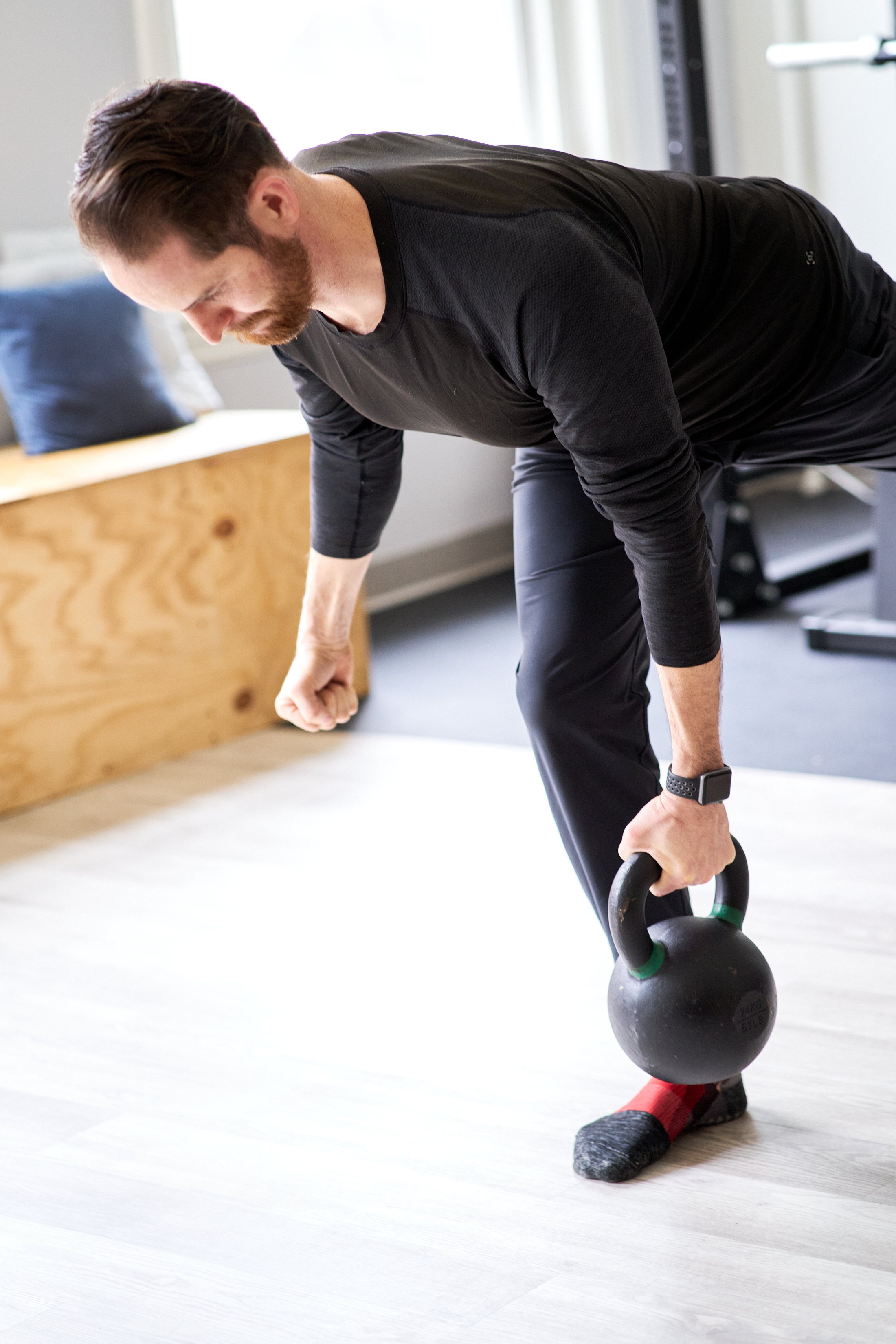 A man in black workout clothes performing a kettlebell exercise in a home gym.