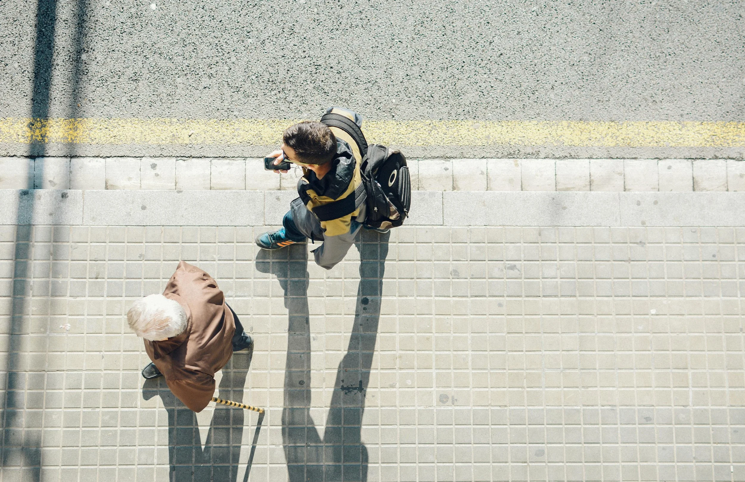 Overhead shot of two people walking on a city sidewalk on a sunny day
