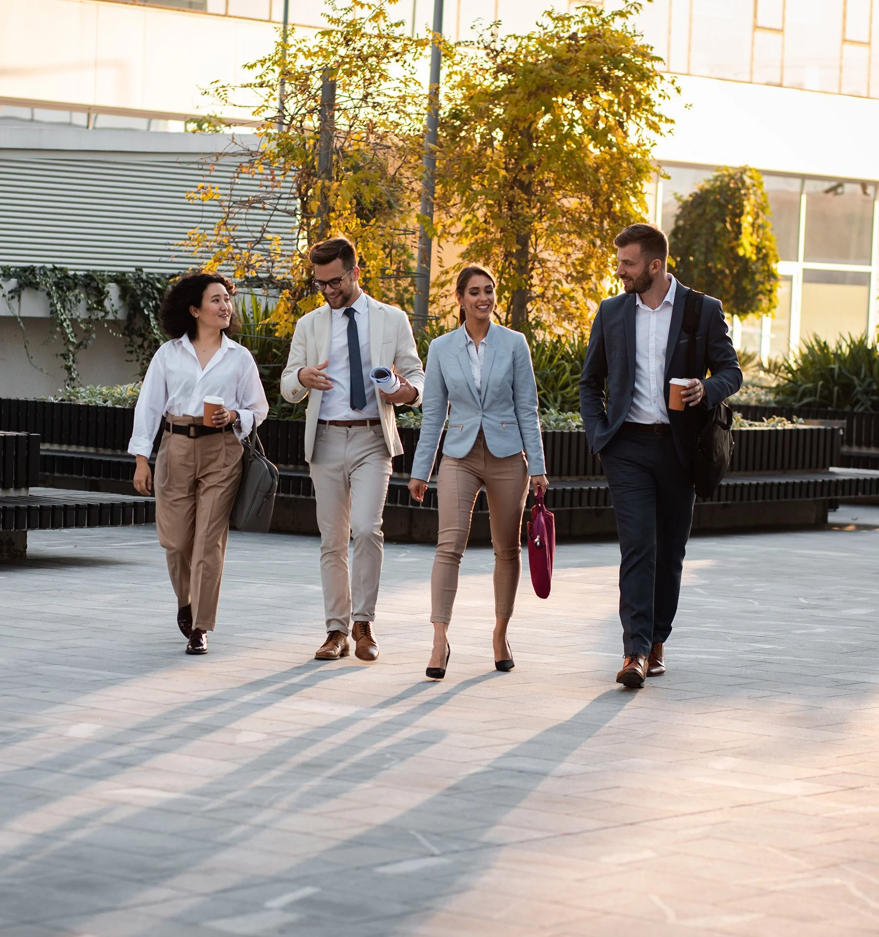 Group of four people in professional business attire walking outside smiling and talking together