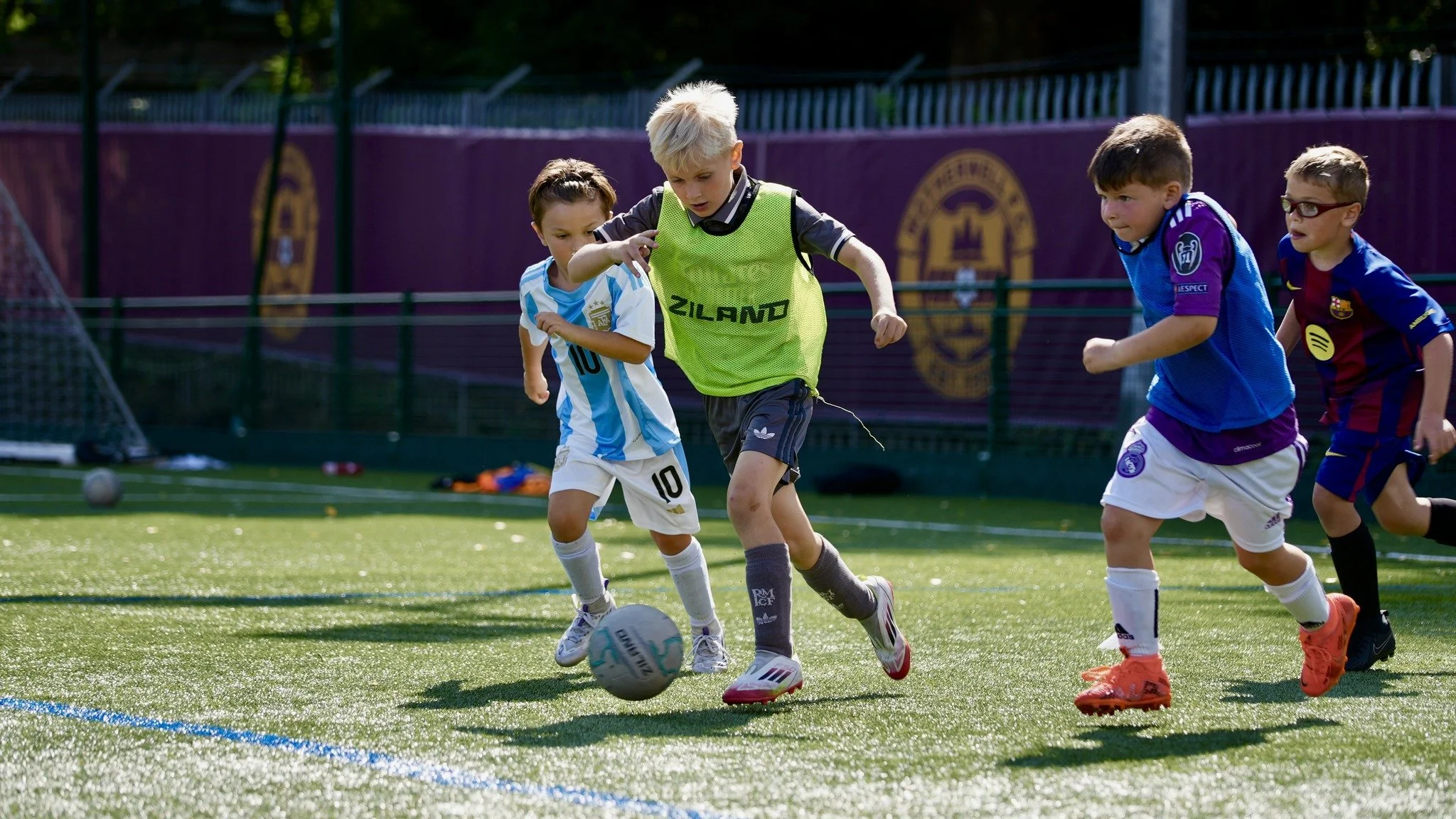 Children playing football on a field, with some kids wearing sports jerseys of different teams.