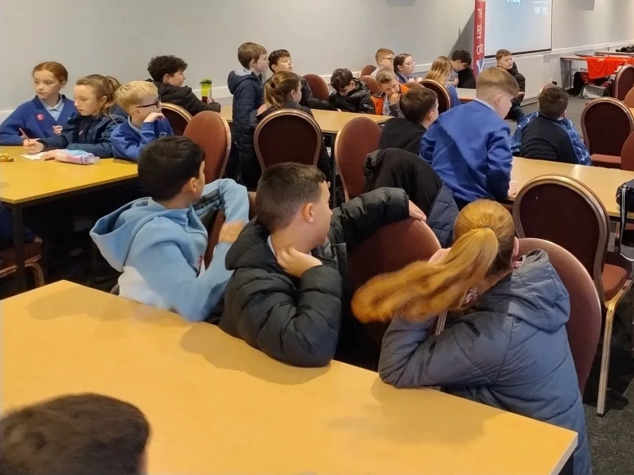 A classroom full of students sitting at desks and listening attentively, with some taking notes and others resting their heads on the desks.