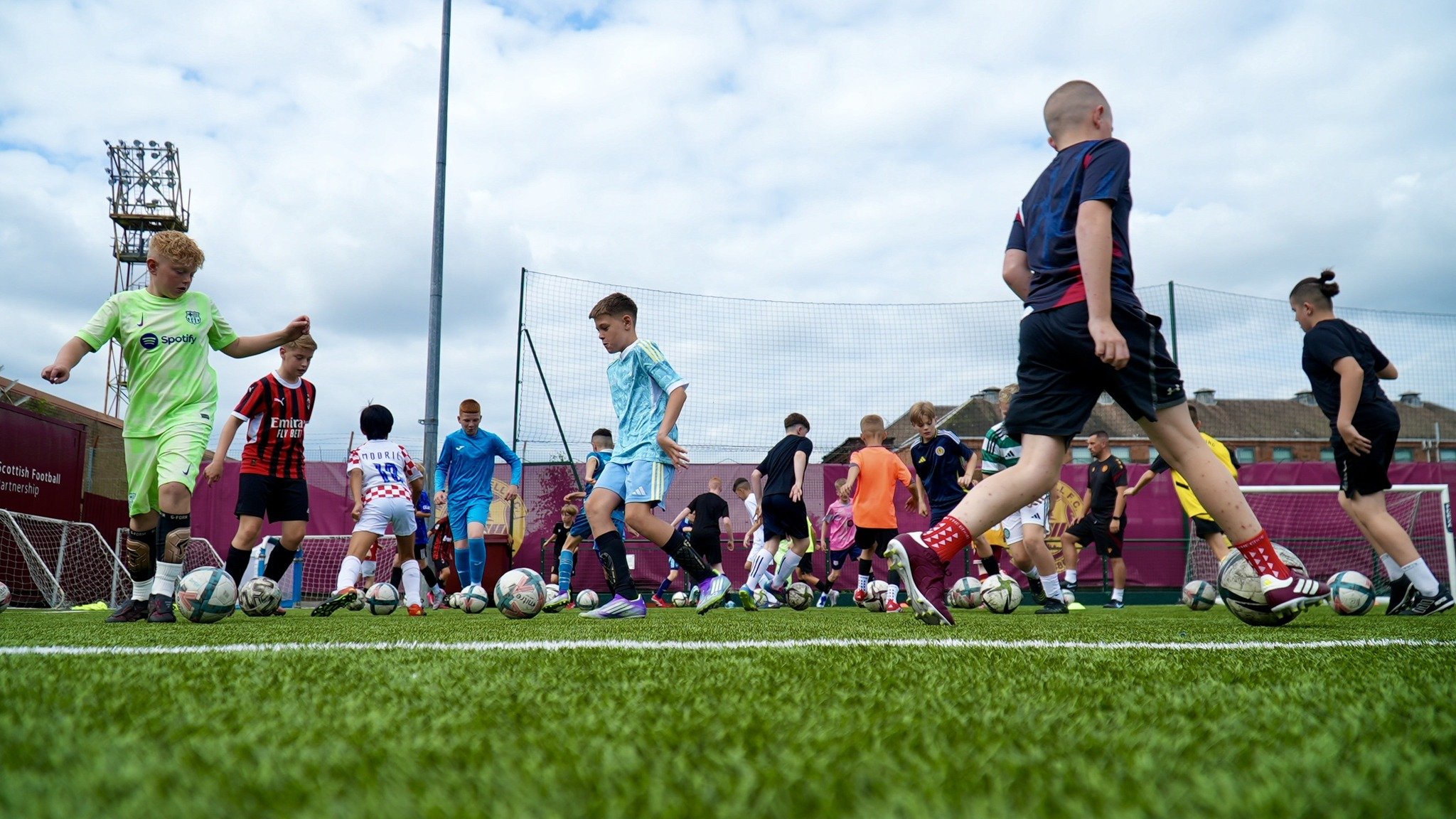 Group of children participating in a football training session on a field with multiple footballs.