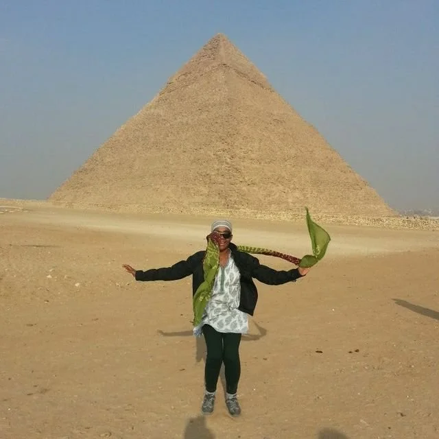 A woman standing in front of a pyramid in Egypt, holding a large green leaf in her hands and smiling.