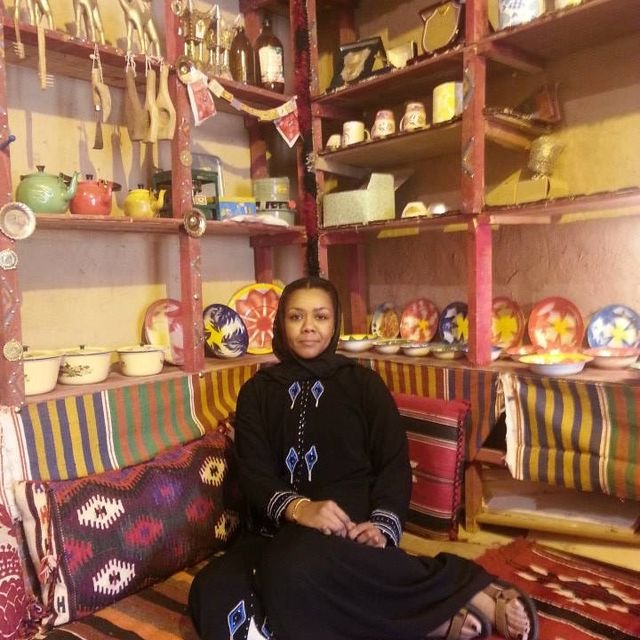 Woman sitting on a colorful, patterned sofa in a room with shelves of ceramics and decorative items.