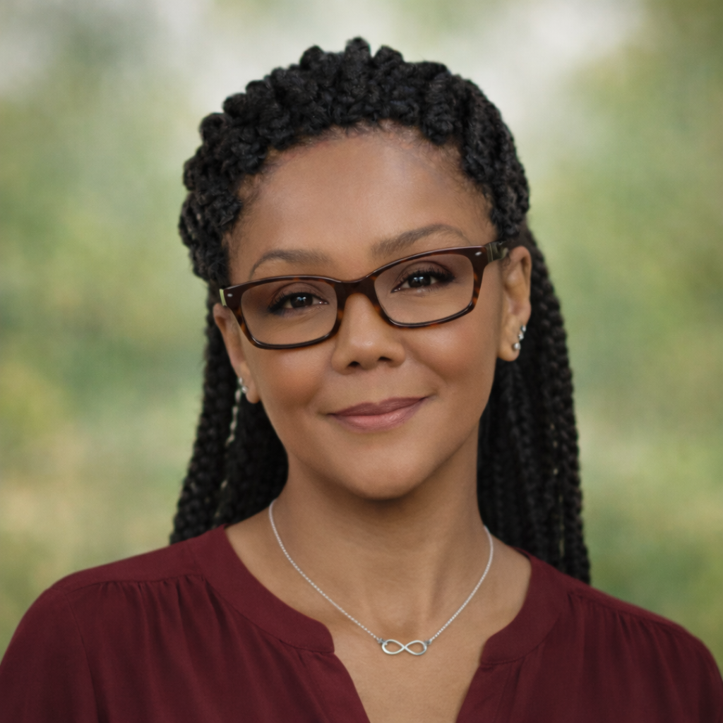 A woman with glasses and braided hair smiling outdoors.