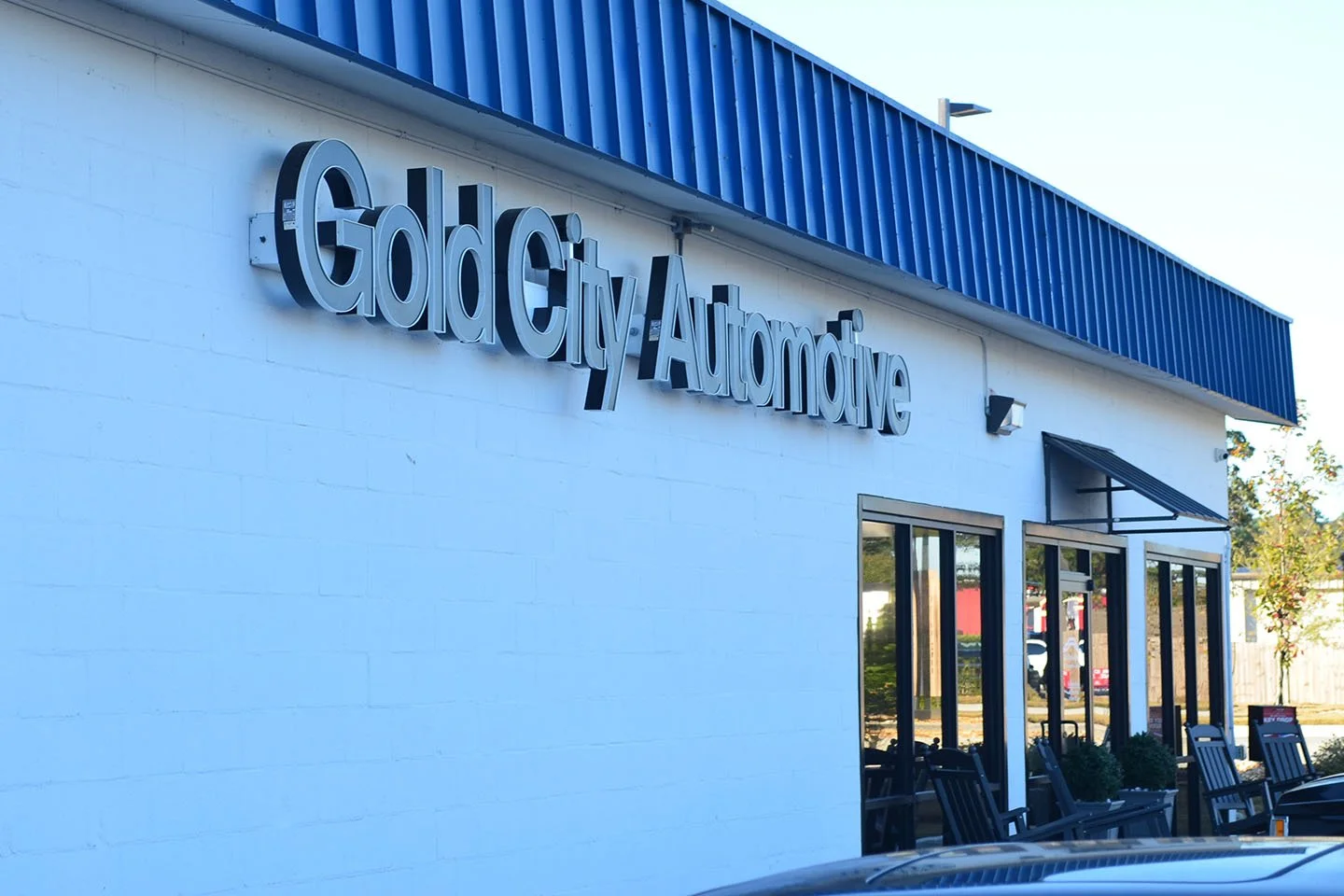Exterior view of Gold City Automotive dealership with glass doors, seating area, and a blue roof.