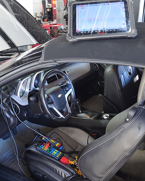Interior of a Chevrolet vehicle with a tablet mounted on the dashboard displaying a diagnostic software, and diagnostic tools connected to the car.