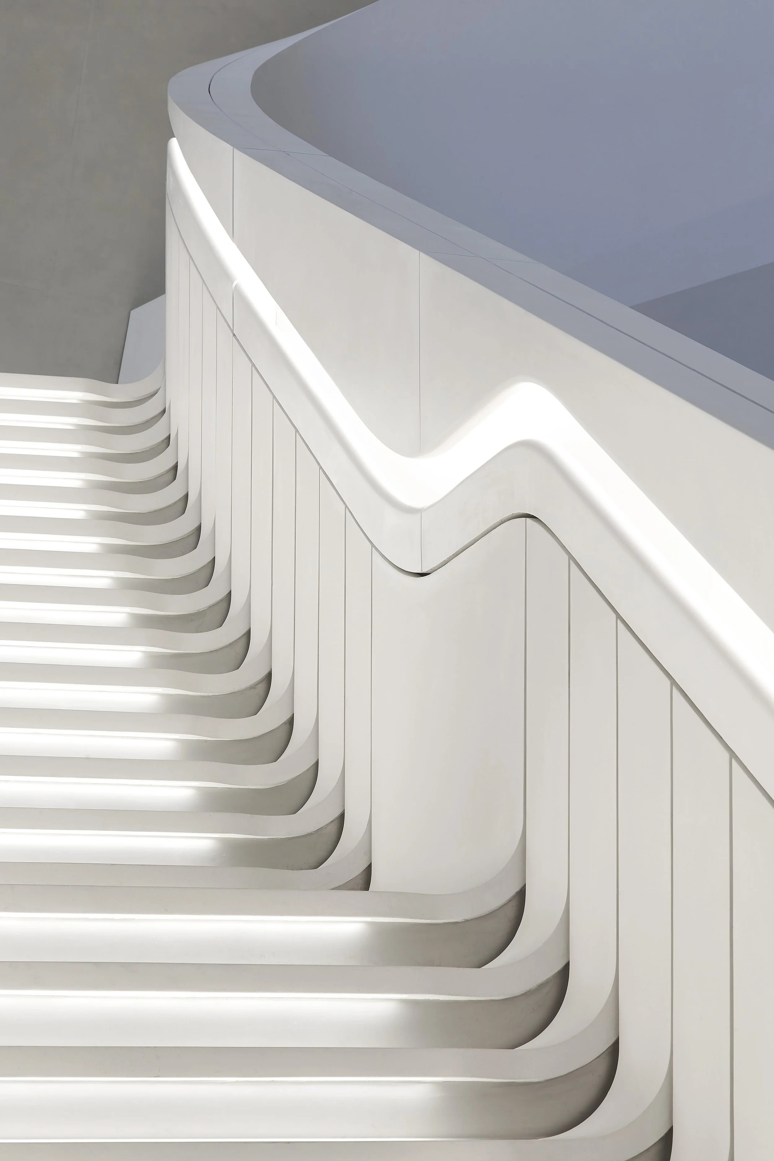 Close-up of a modern white staircase with rounded edges and layered steps, alongside a sleek white railing.