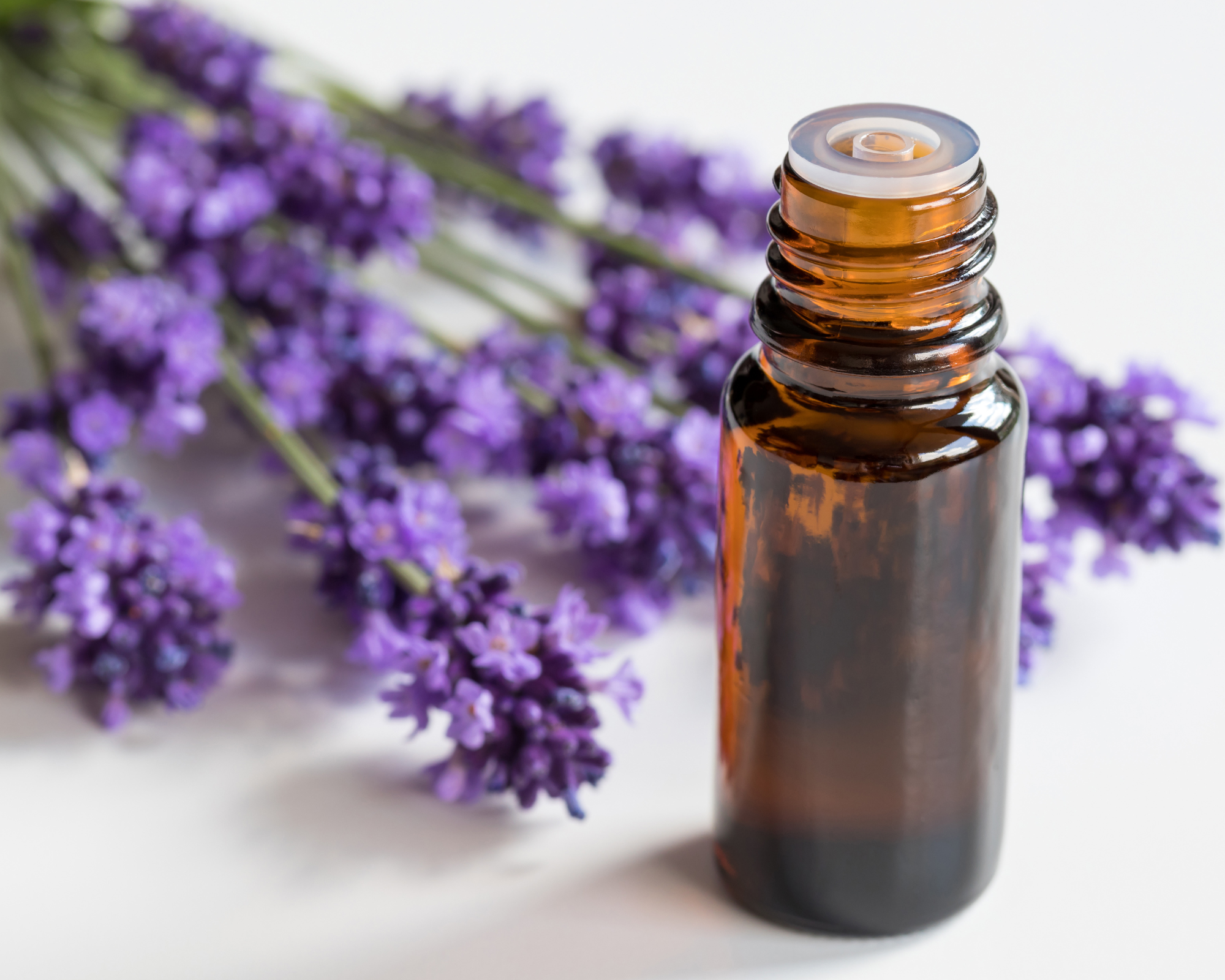 A small amber glass bottle of essential oil with purple lavender flowers in the background.