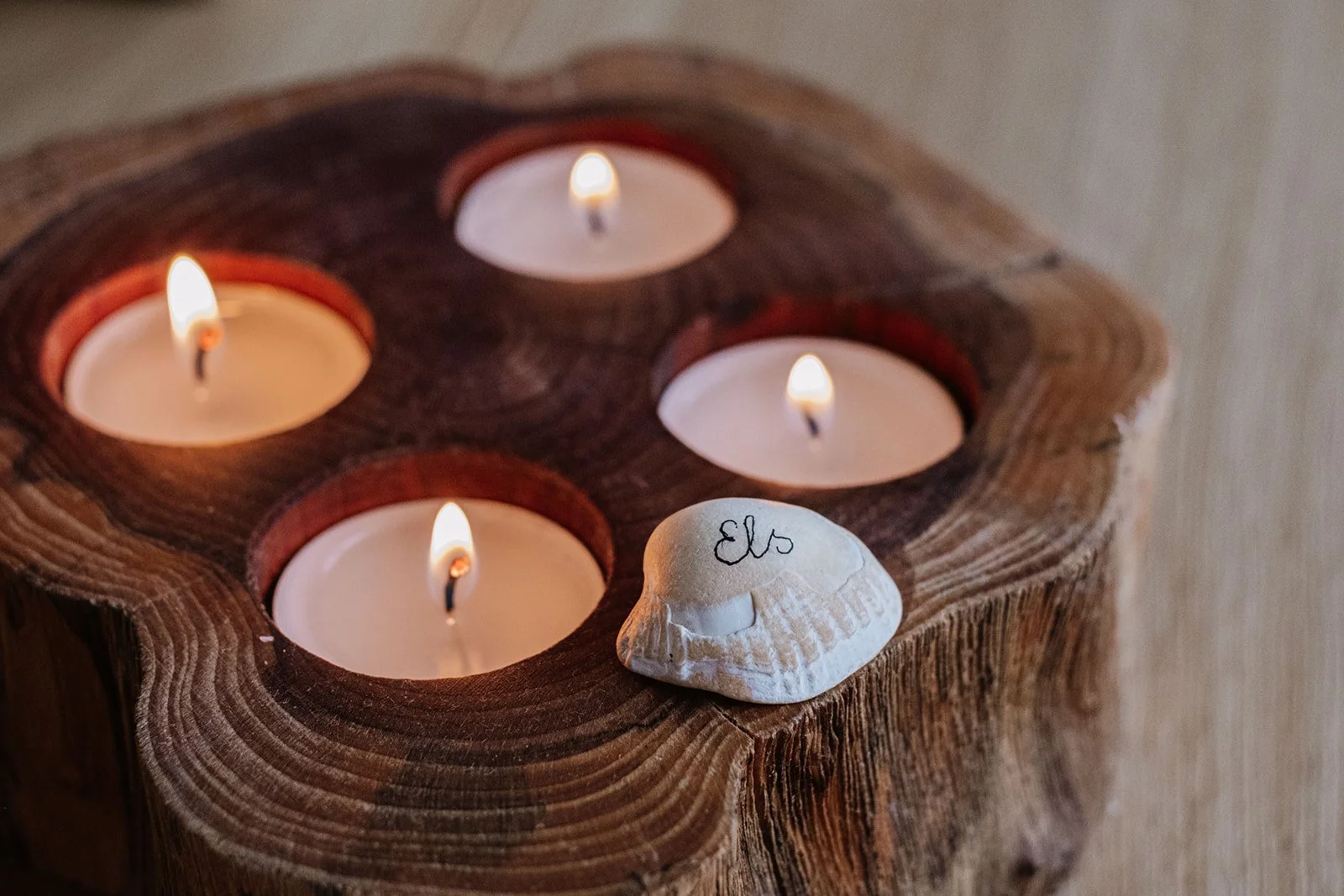 Vier brandende kaarsen in een houten kandelaar met een schelp met het woord 'Els' erop.