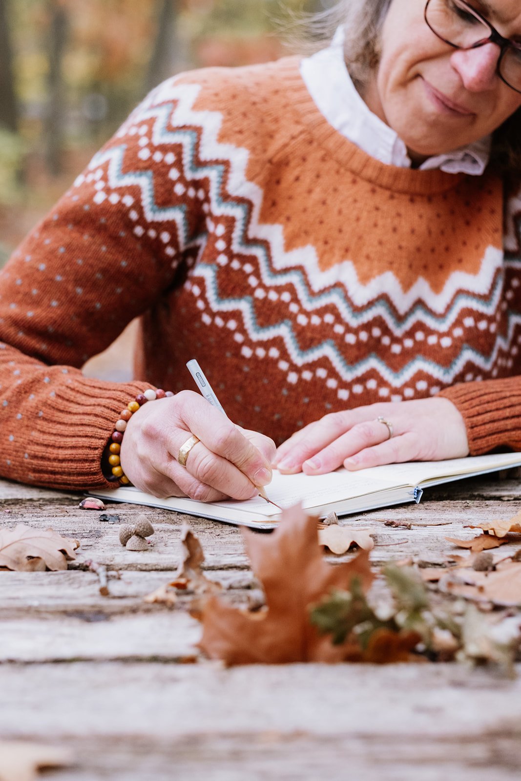 Vrouw schrijft in een open notitieboekje op een rustiek houten tafel in een herfstbos, omringd door bladeren en paddenstoelen.