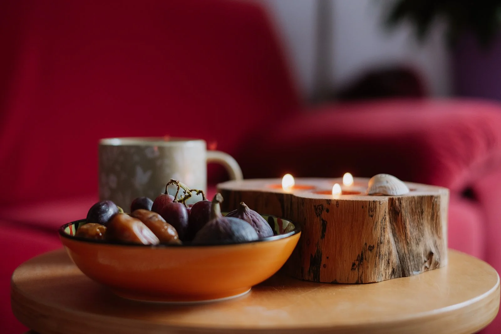 Fruitcombinatie van druiven, vijgen en dadels, samen met een mok en een houten kaarsenhouder met brandende kaarsen op een houten tafel.