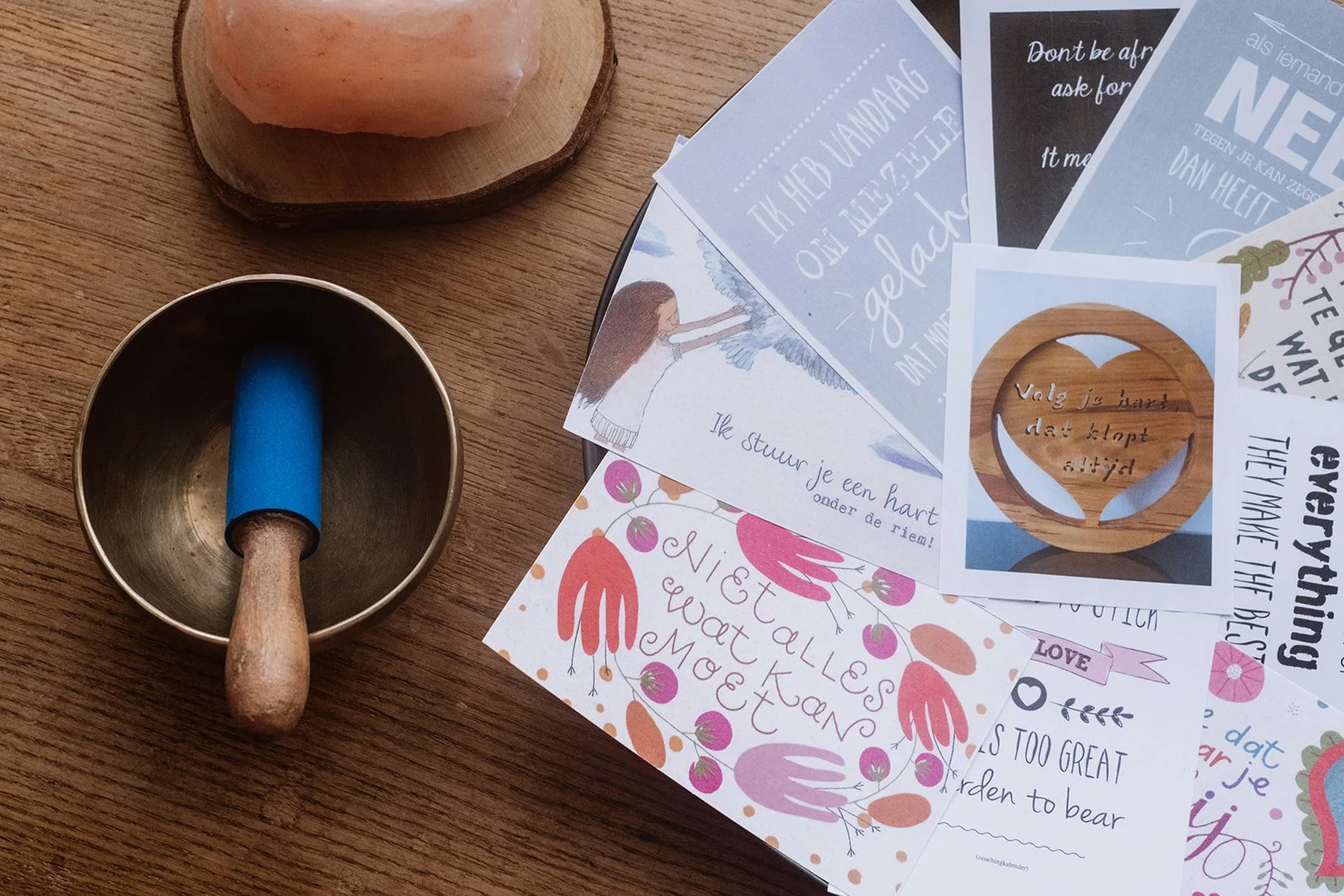 Een koperen schaaltje met een blauwe afsluitdop en een houten handvat, naast een houten bord en meerdere vellen papier met inspirerende teksten en illustraties.