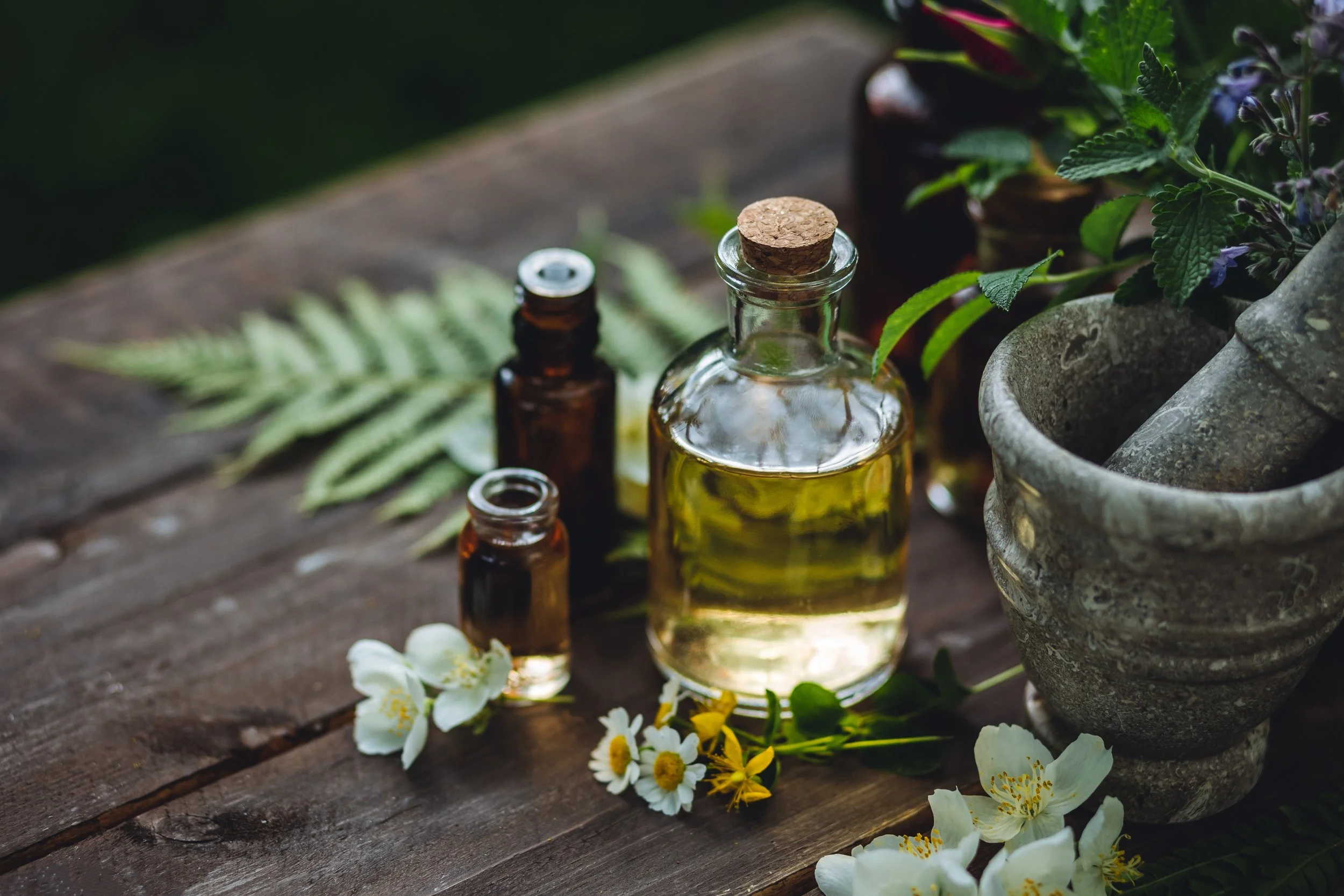 Herbal medicine and essential oils in glass bottles on a wooden table with flowers and green foliage.