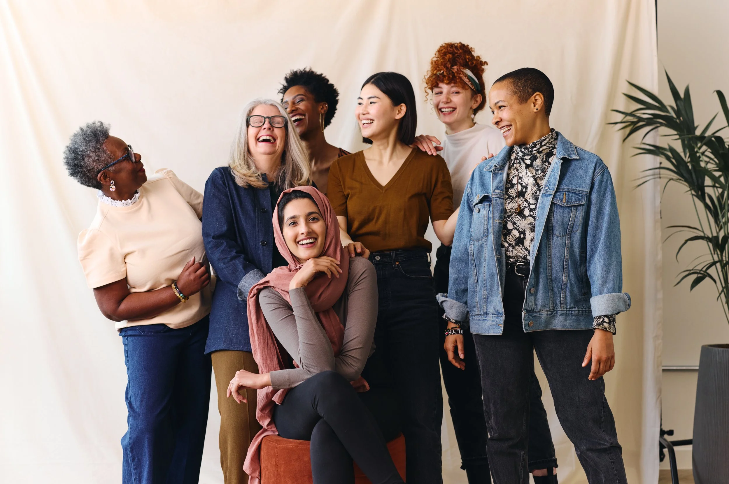 Group of diverse women laughing and smiling together in a casual indoor setting.