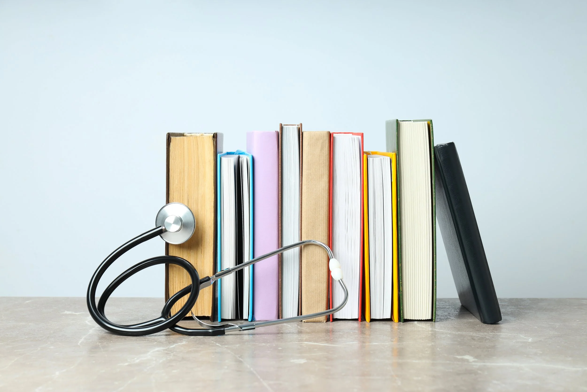 A stethoscope resting on a row of colorful books on a table.