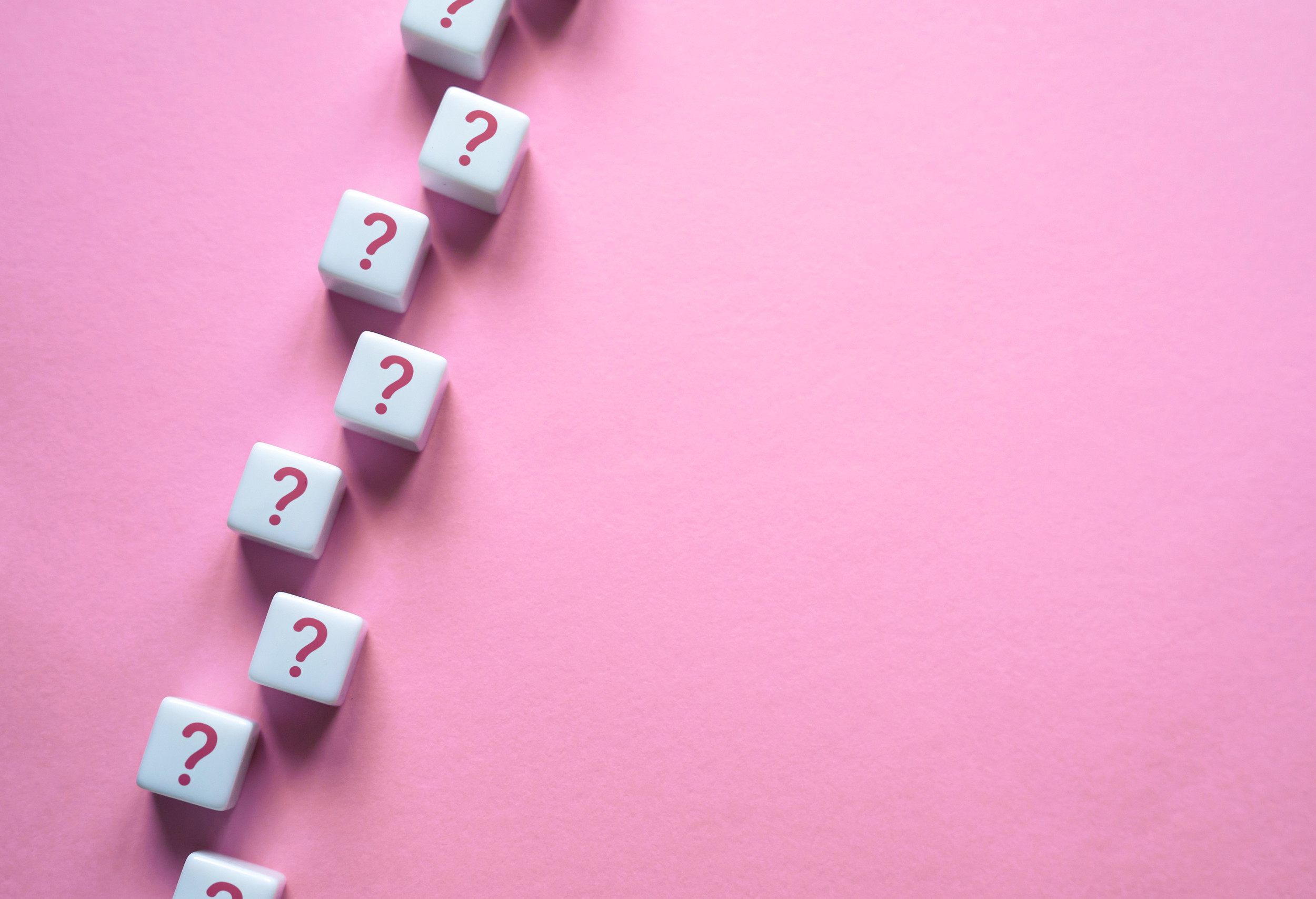 Multiple white dice with pink question marks, arranged in a diagonal line on a pink background.