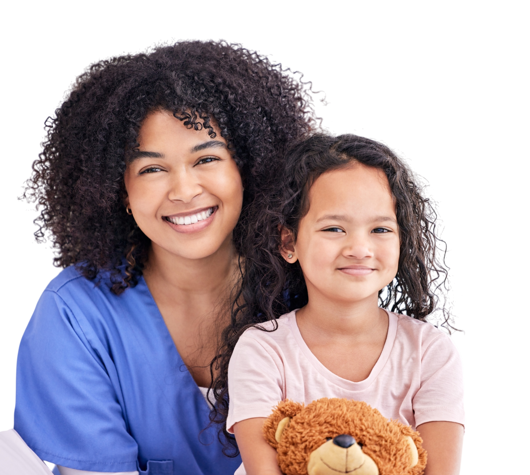 A smiling woman with curly hair wearing blue scrubs sitting next to a girl with curly hair holding a teddy bear.
