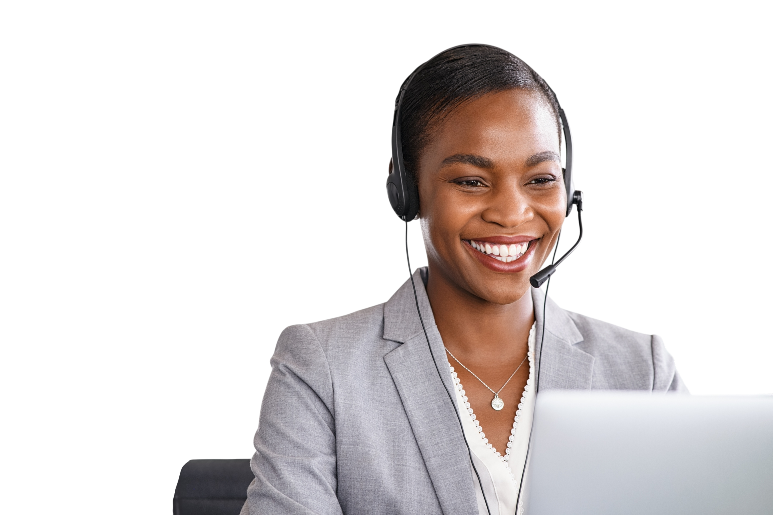 A smiling woman wearing a headset and gray blazer working at a laptop.