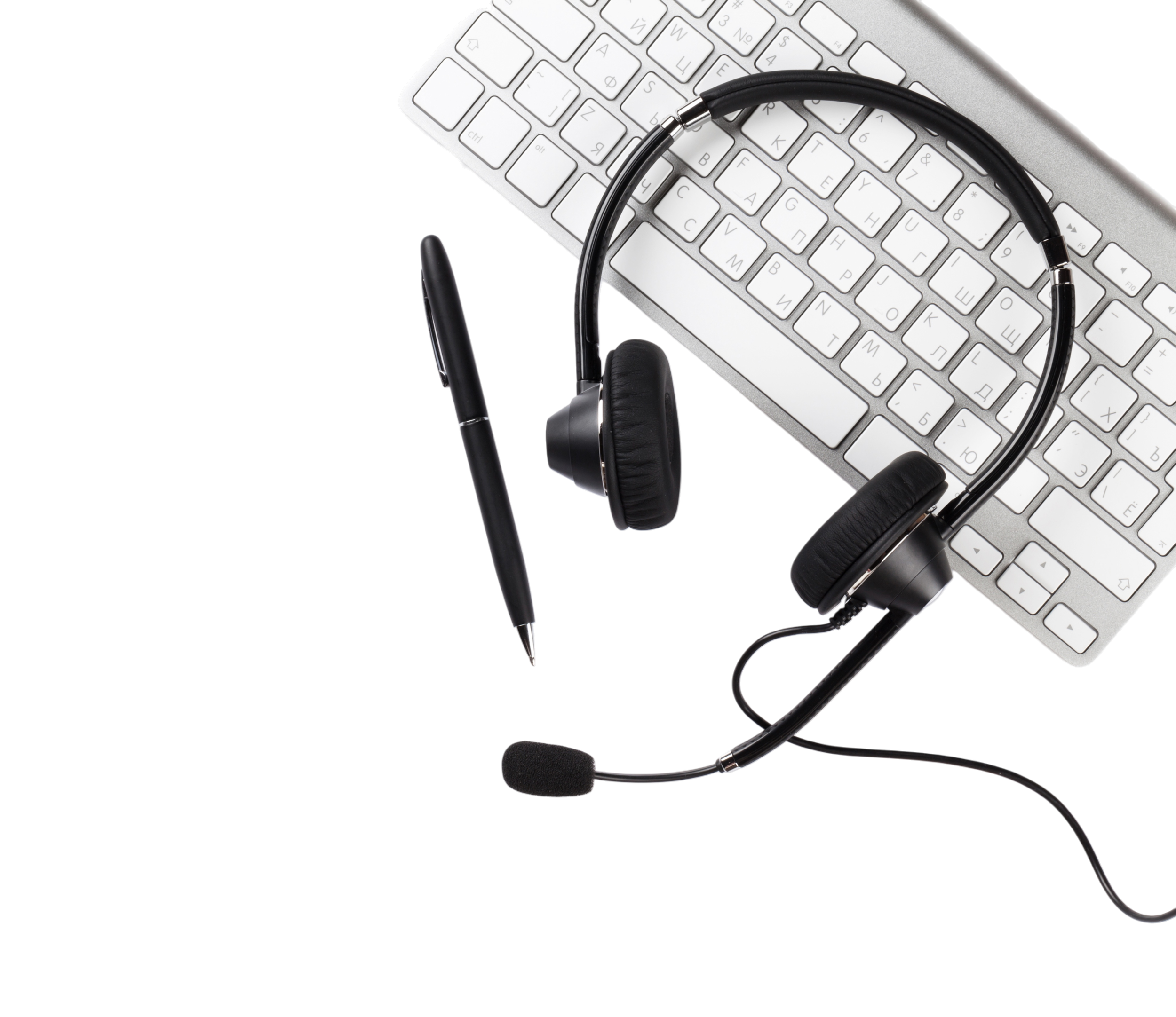 A black headset with microphone, a pen, and a white computer keyboard on a black surface.