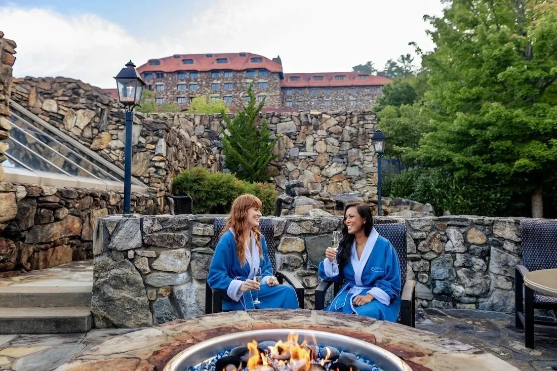 Two women in blue spa robes sharing wine around an outdoor fire pit at the Grove Park Inn  Spa.