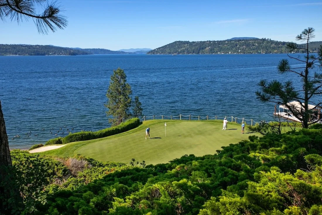 Golfer putting on a lakeside green at the Coeur d’Alene Resort Golf Course with forecaddie and playing partner nearby.