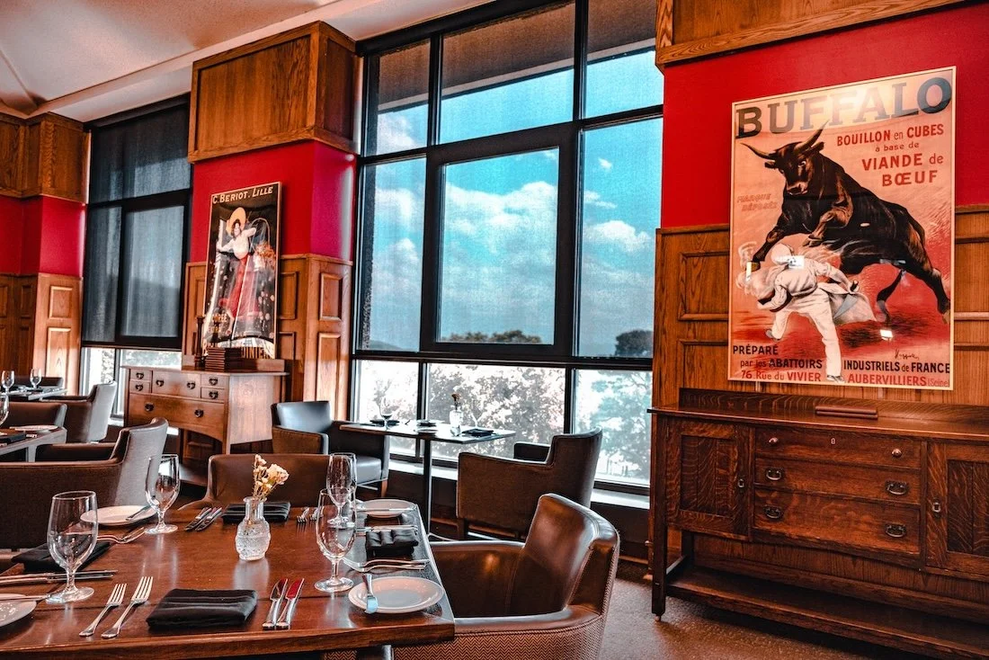 Set tables and wood features in the Grove Park Inn’s Vue 1913 dining room with vintage posters flanking a picture window.