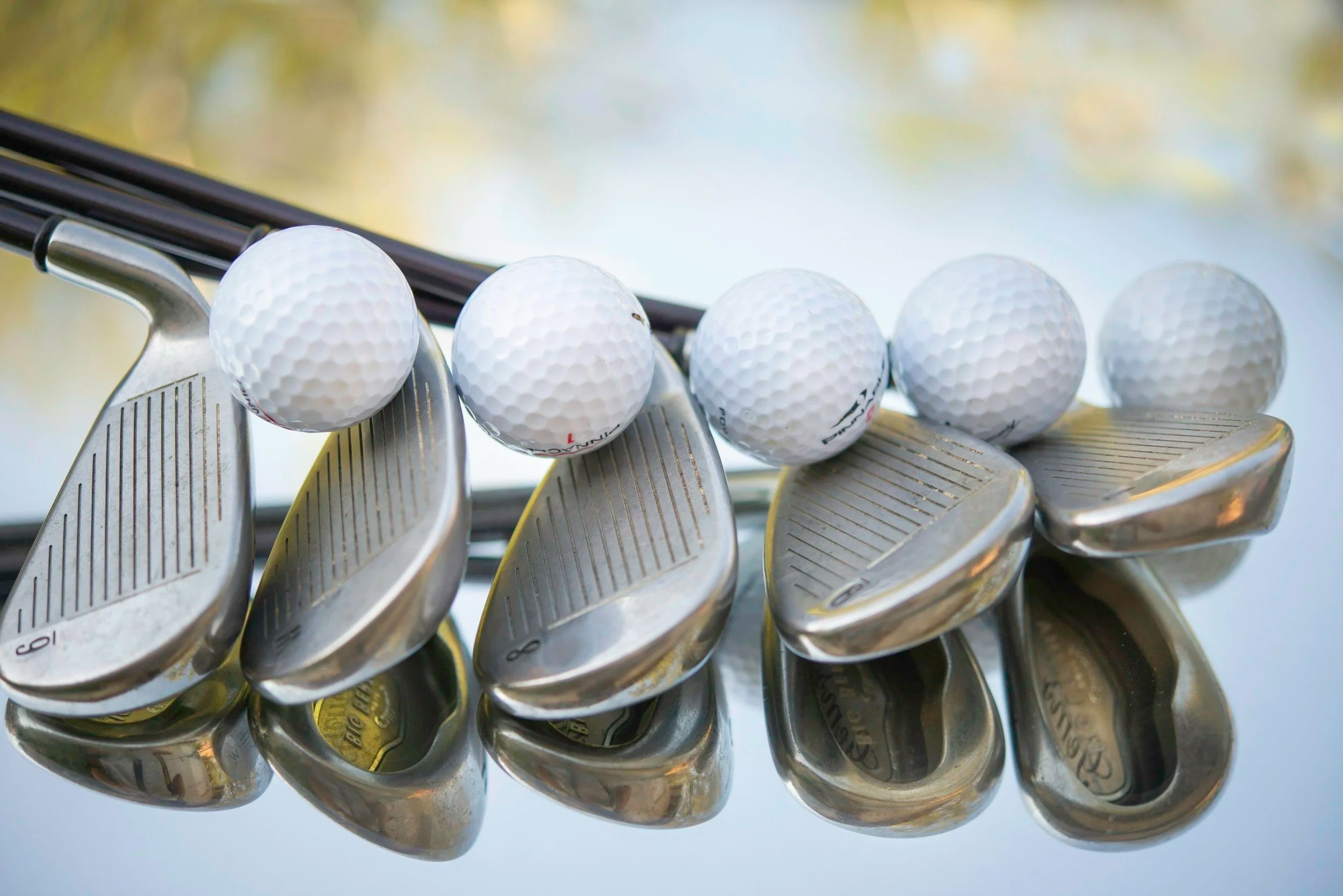 Five golf balls balanced on the heads of five iron golf clubs