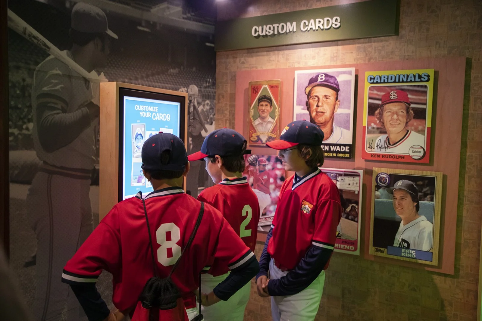 Three boys in baseball uniforms look at a card exhibit at the Baseball Hall of Fame.