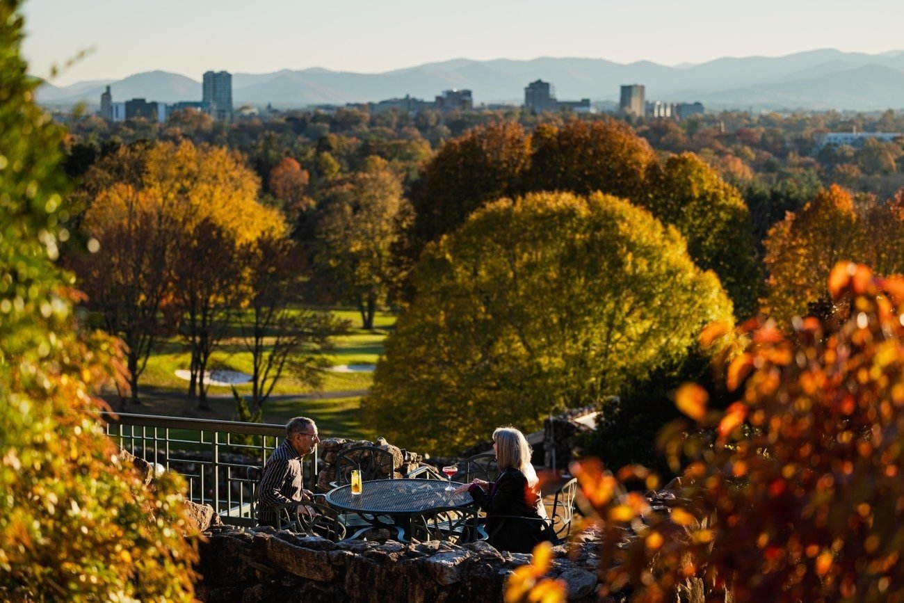Couple enjoying drinks on the Grove Park Inn’s Sunset Terrace above the golf course with downtown Asheville in the distance.