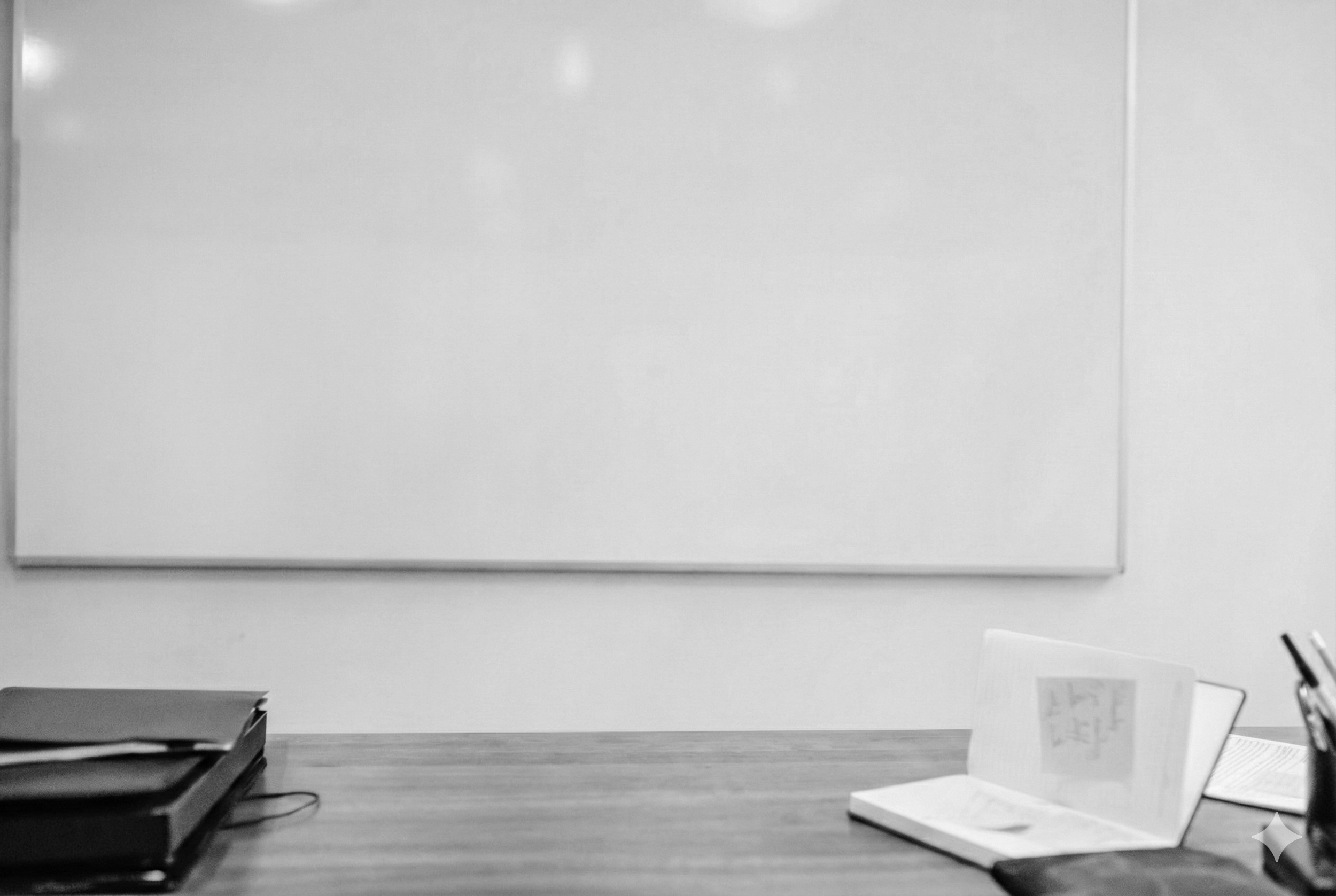 Empty whiteboard on a wall above a wooden desk, with notebooks, papers, and a pen holder on the desk.