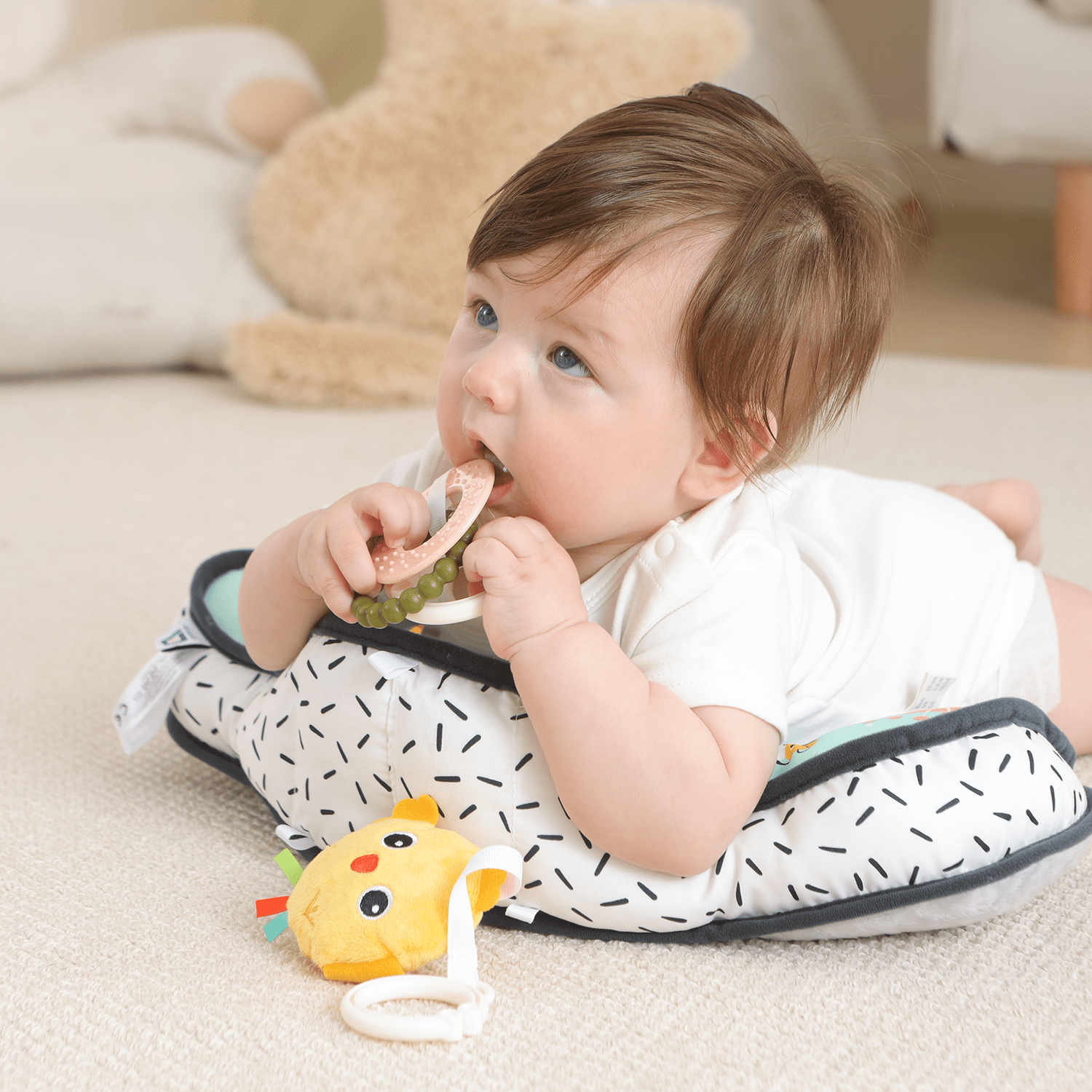 Baby doing tummy time on a Lovvie & Joy support pillow while chewing a teether